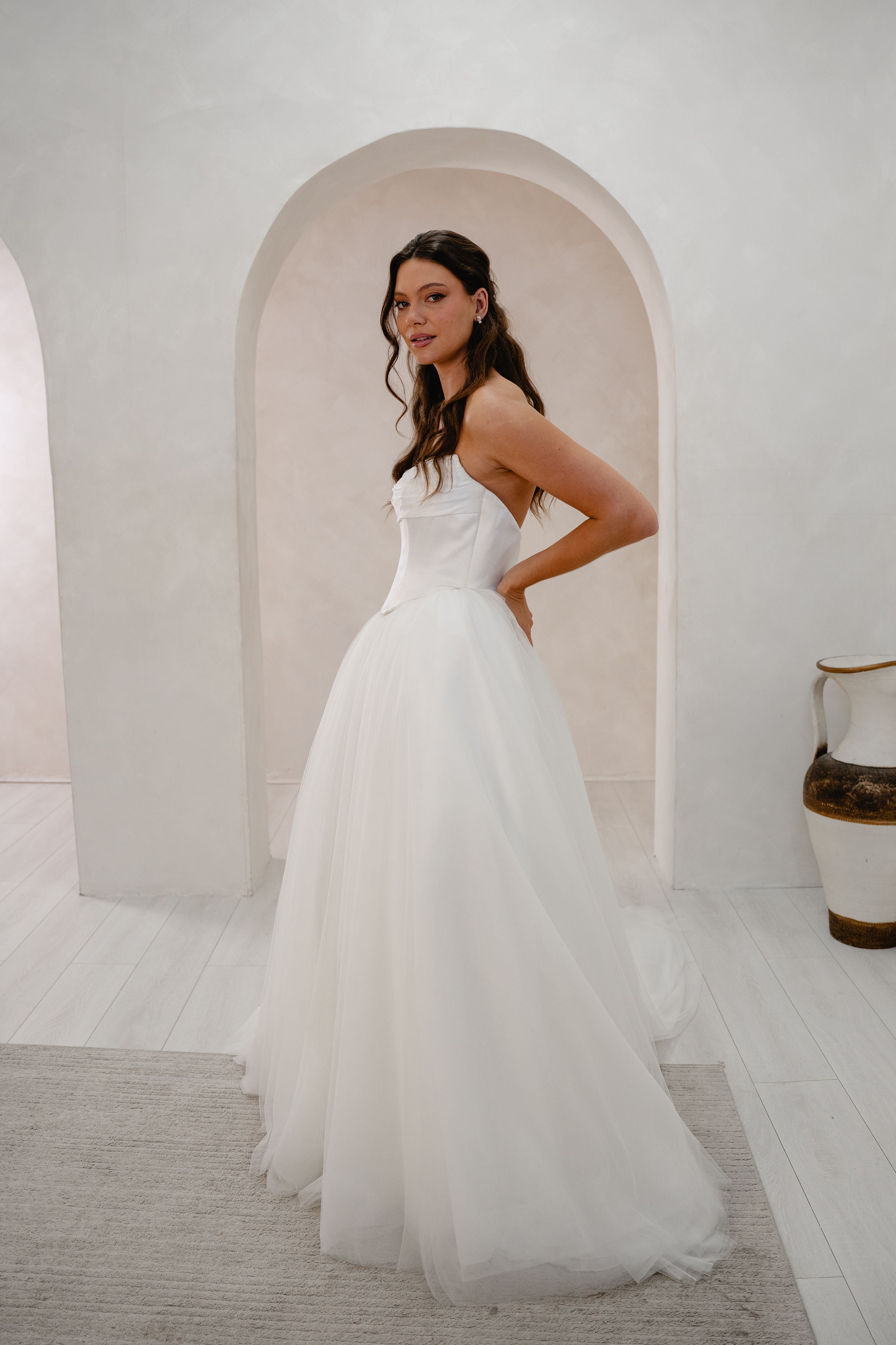 Woman in a white wedding dress standing in a softly lit room with arches.