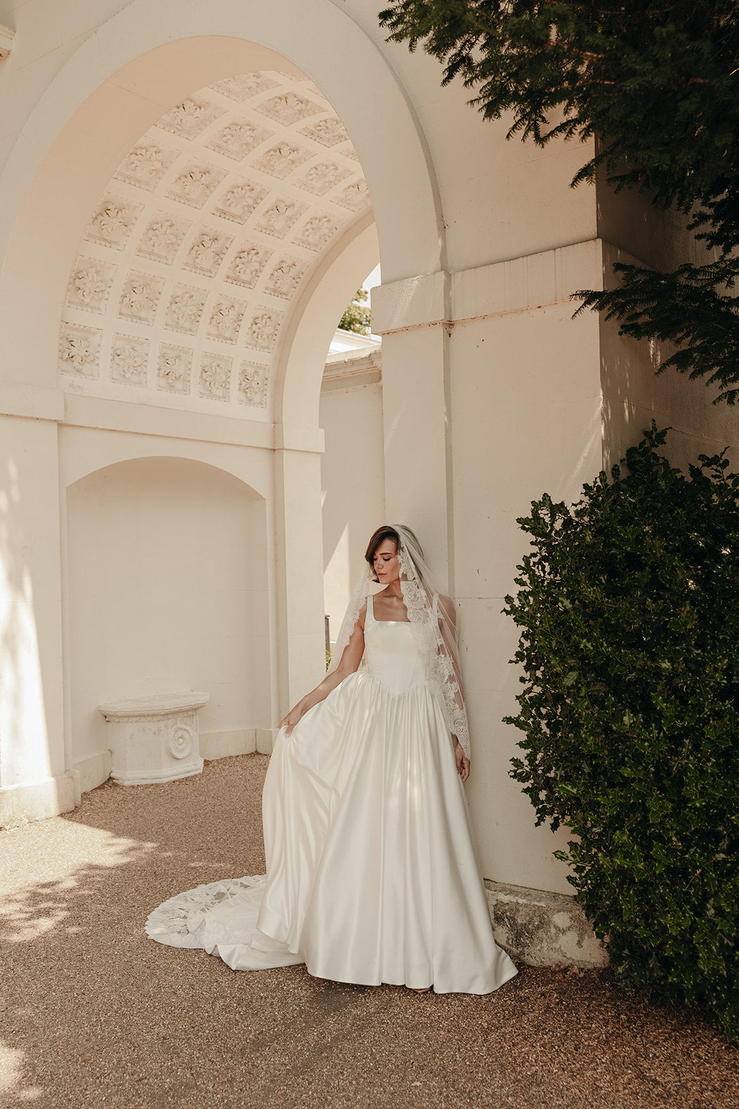 Bride in a ivory wedding dress standing under an archway with greenery.