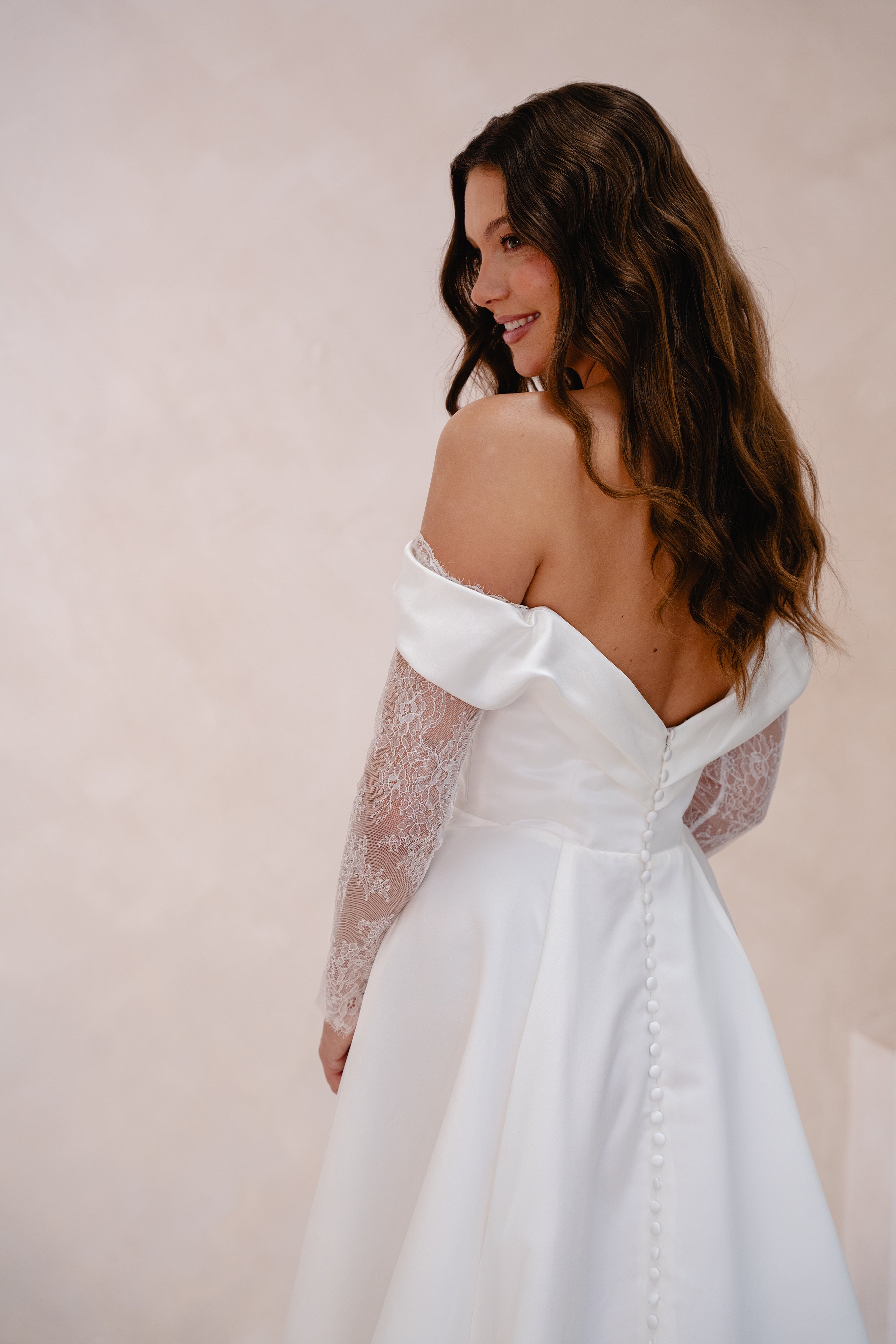 Woman wearing a white off-shoulder dress with sheer lace sleeves against a plain background