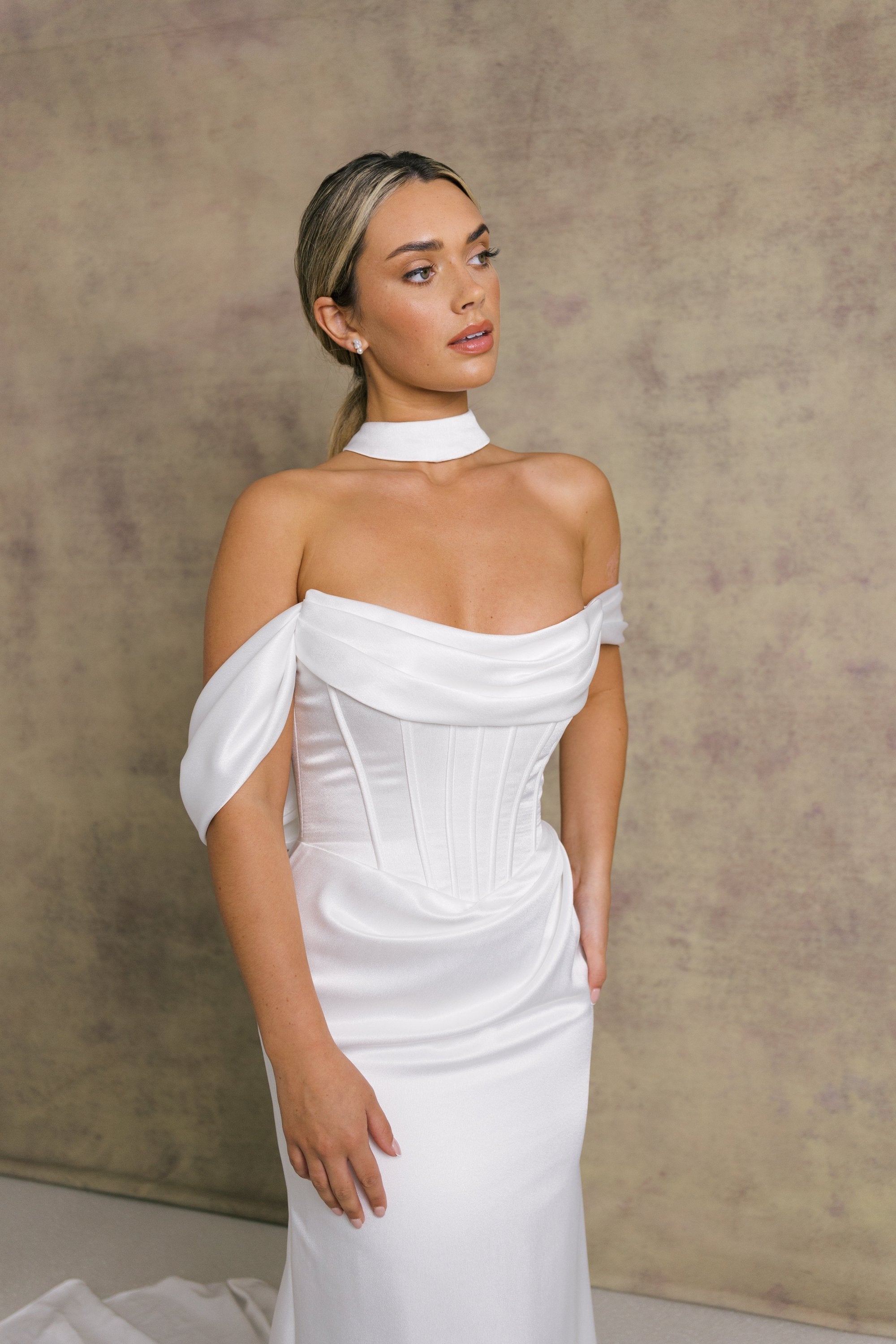 A woman in luxurious slipper satin wedding dress featuring a draped neckline on an exposed boned corset style drop waist bodice with draped bardot’s on our new ruched skirt.