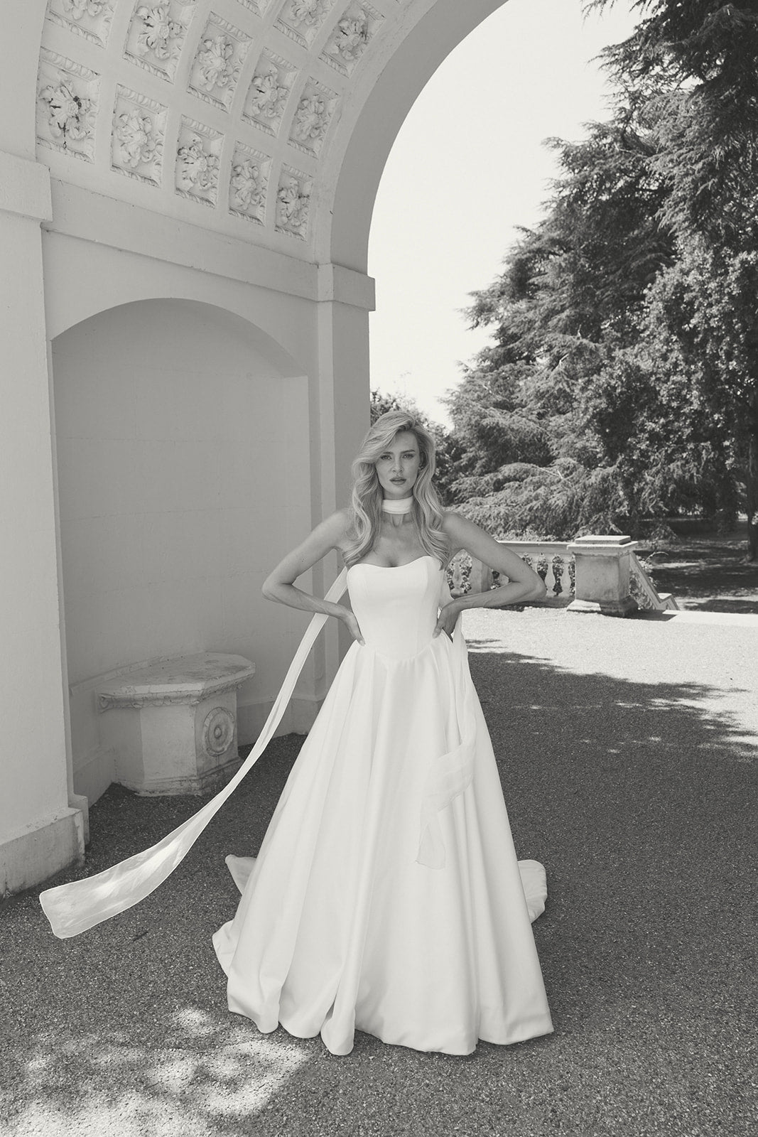 Woman in a strapless ivory wedding dress with a long train standing in a garden setting.