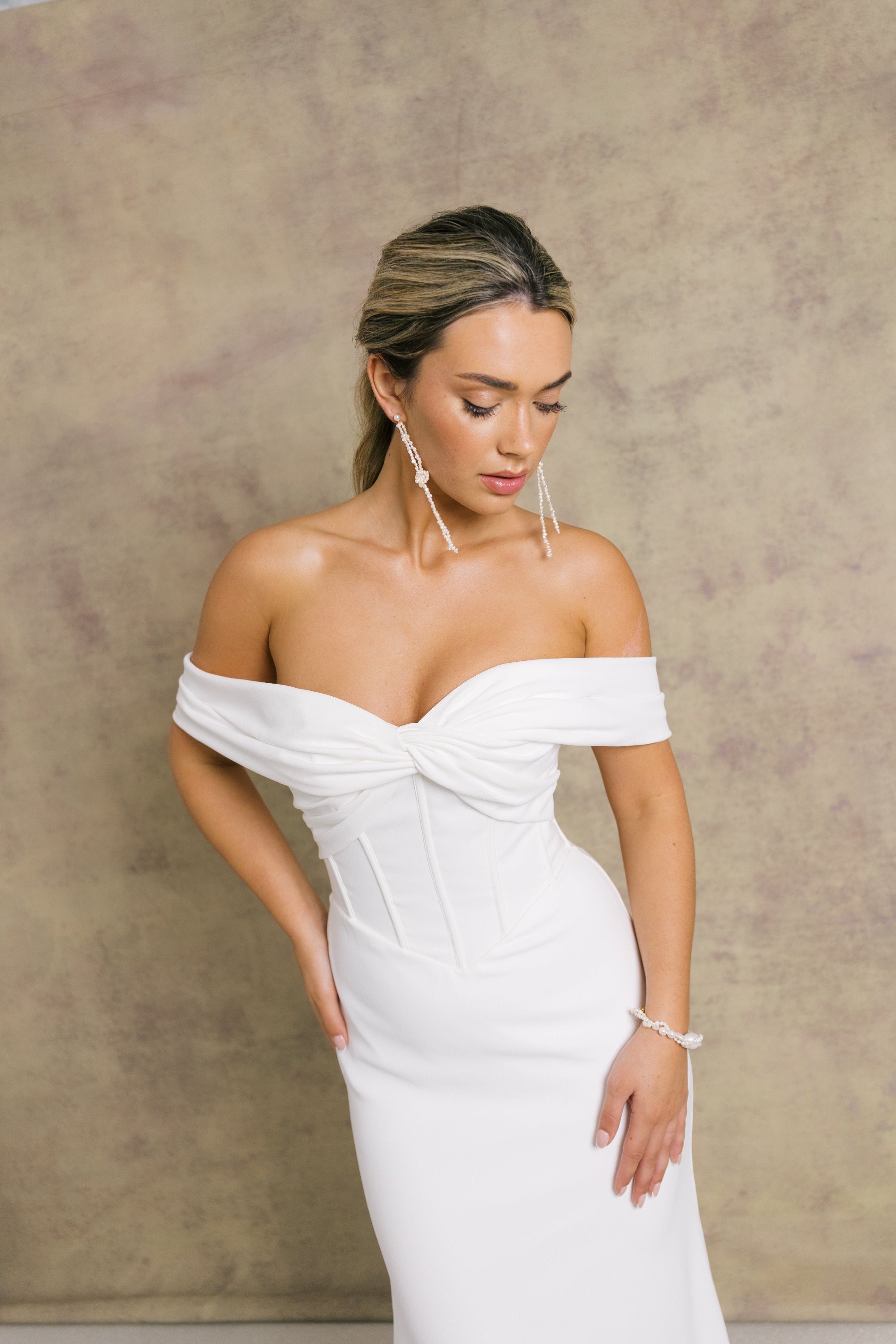 A woman in a gorgeous off shoulder sweetheart dropped waist wedding dress, featuring exposed boning on a crepe fit and flare skirt.
