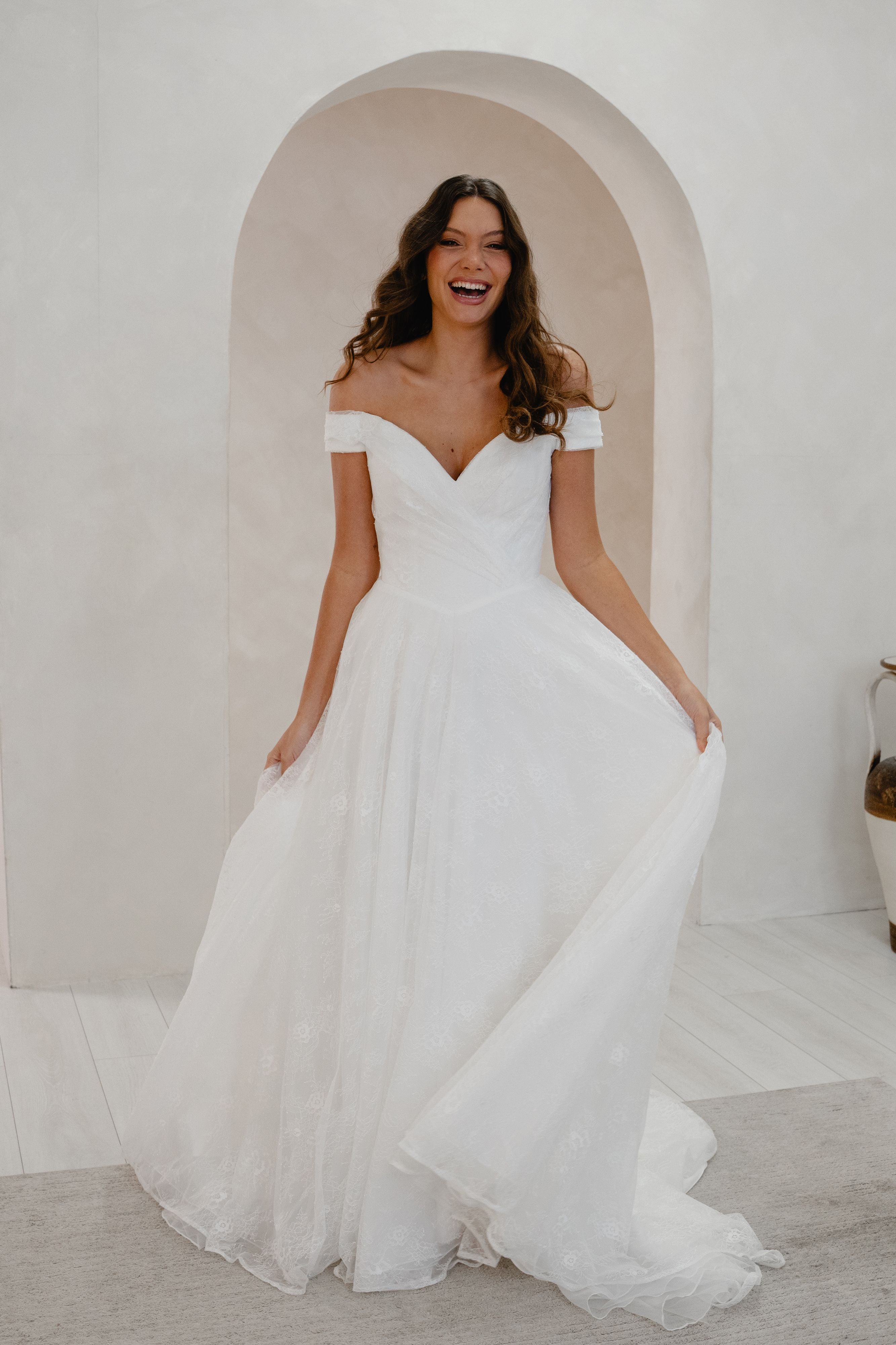 Woman in a white wedding dress standing in a room with arched doorways.
