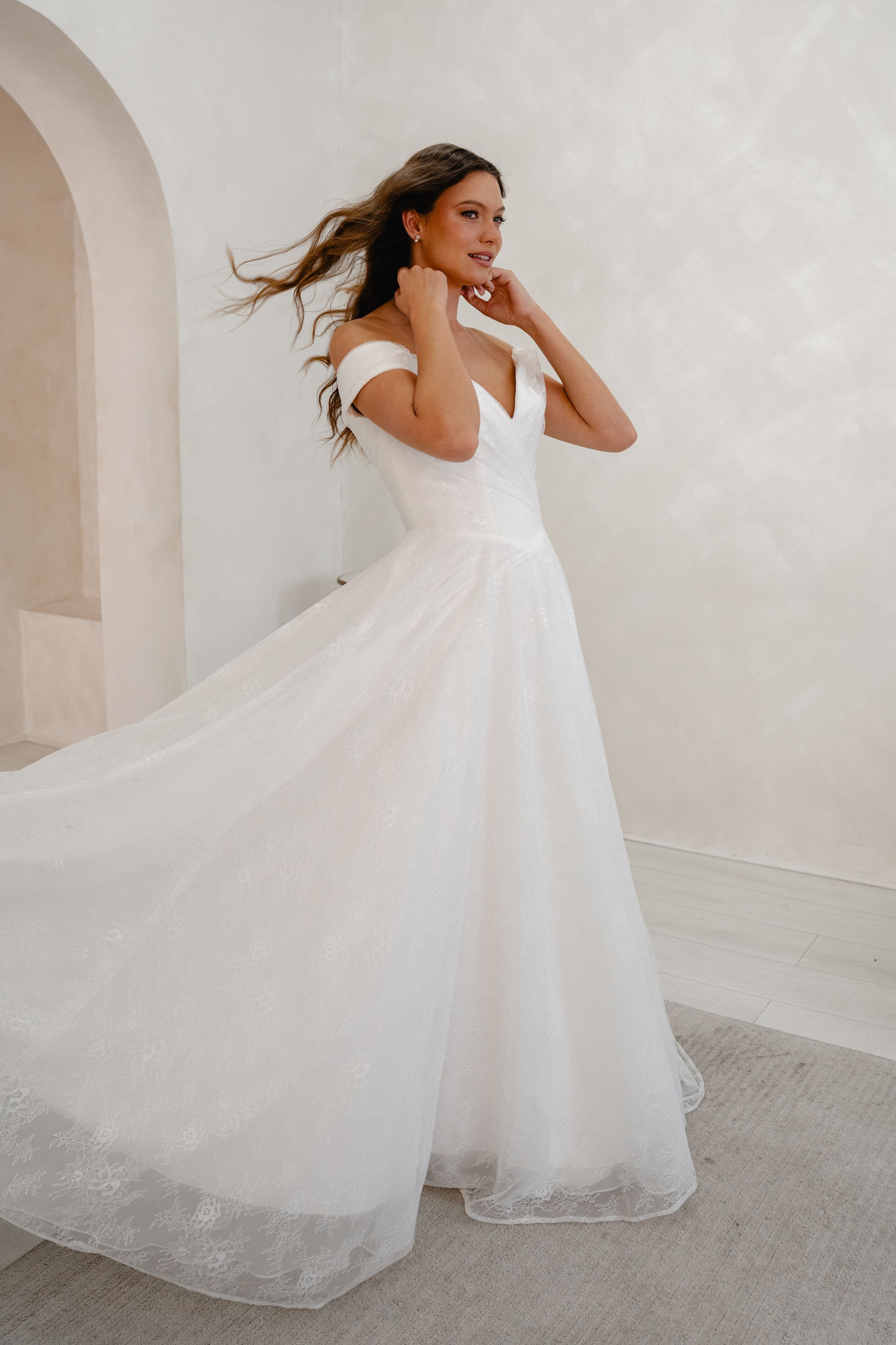 Woman in a white wedding dress standing in a minimalistic room with a white wall and gray floor.