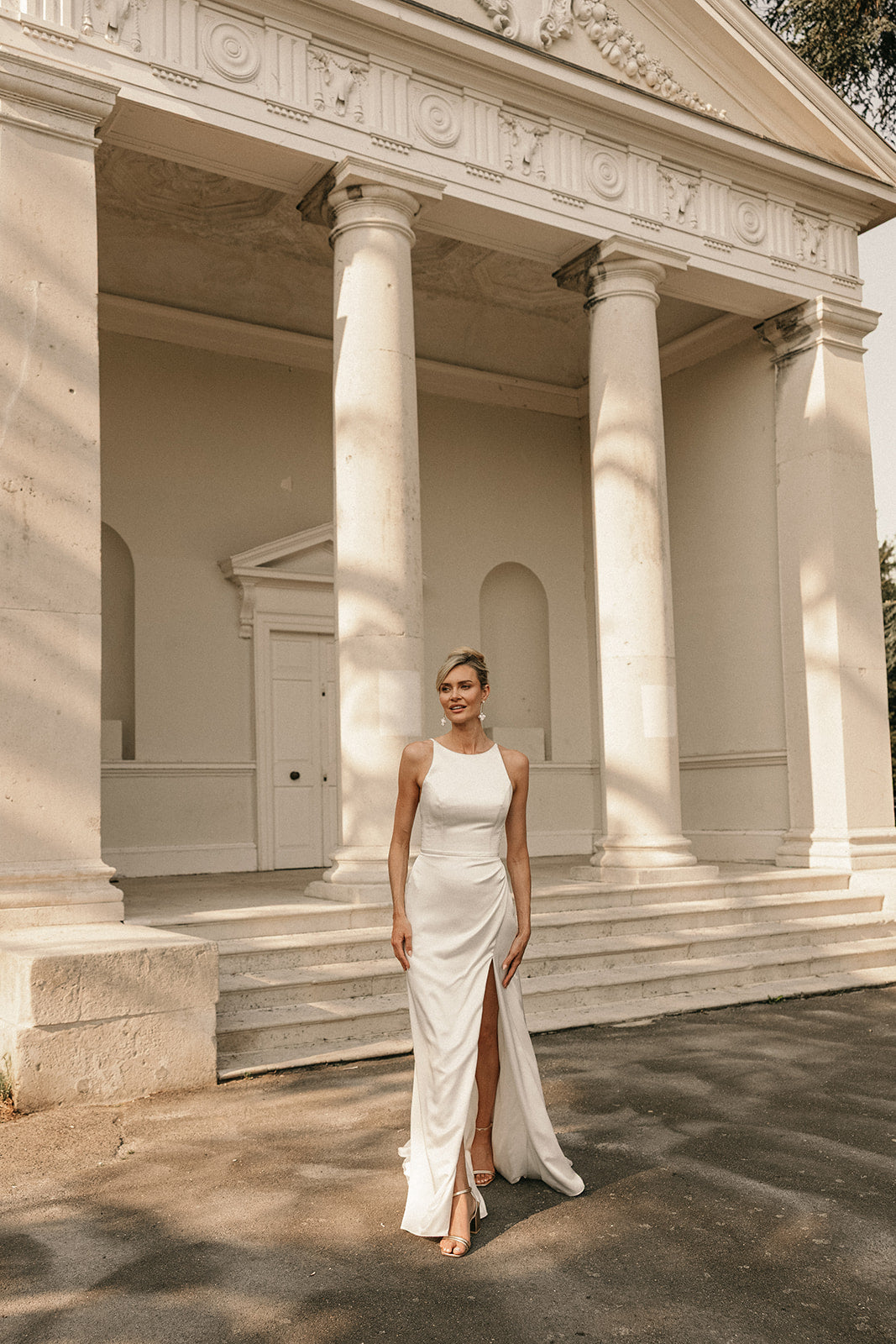 Woman in a ivory slipper satin wedding dress standing in front of classical architecture