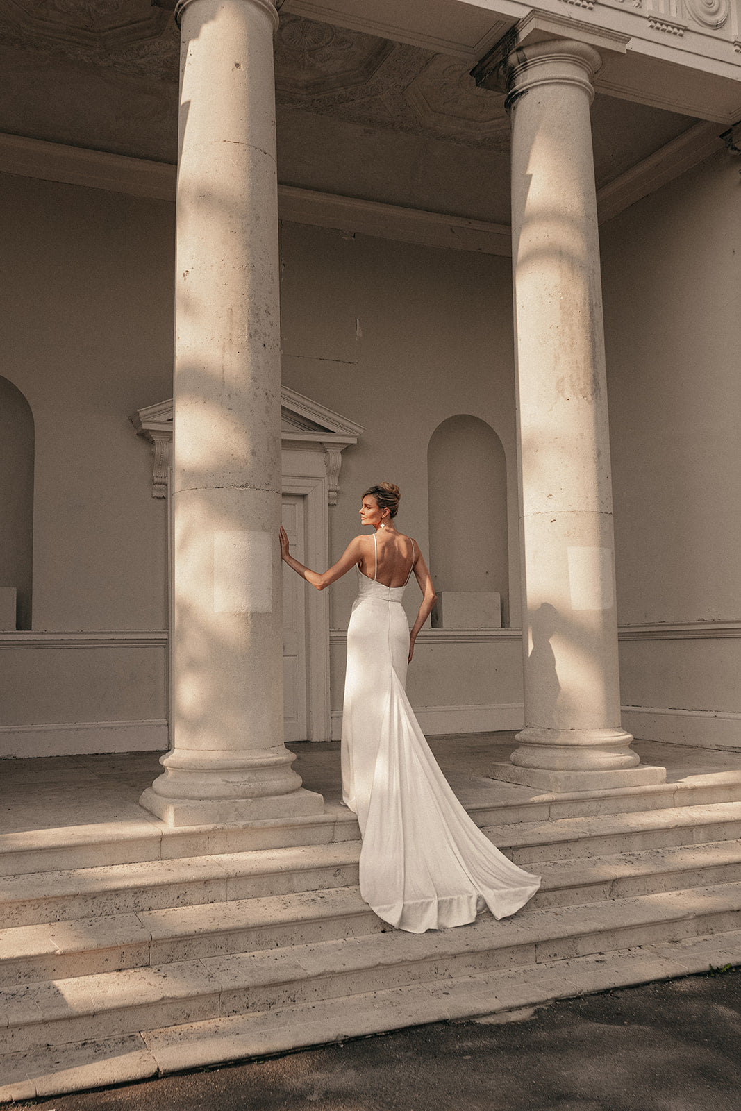 Woman in a ivory wedding dress standing on steps with classical columns in the background