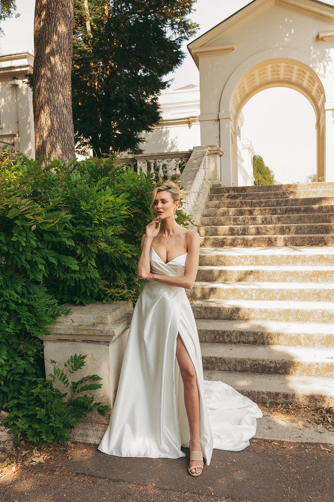 Woman in a ivory satin wedding dress standing on stone steps with classical architecture in the background.