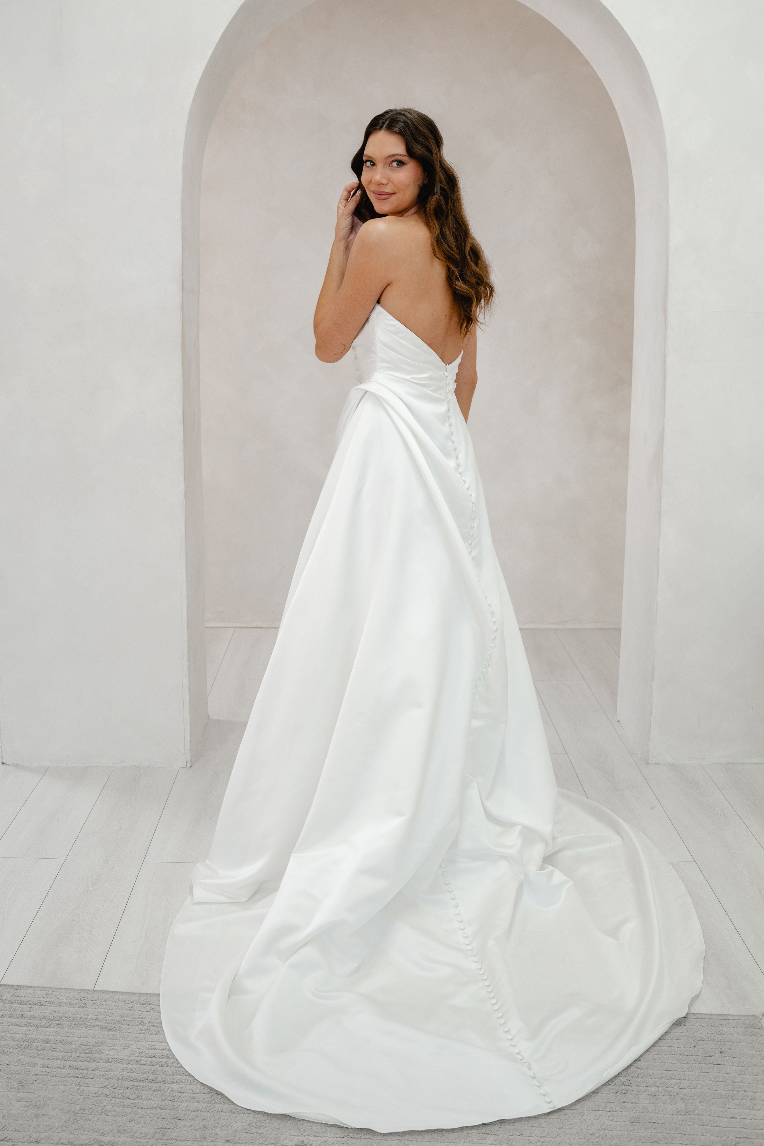 Woman in a white wedding dress standing in a minimalistic room with an archway.