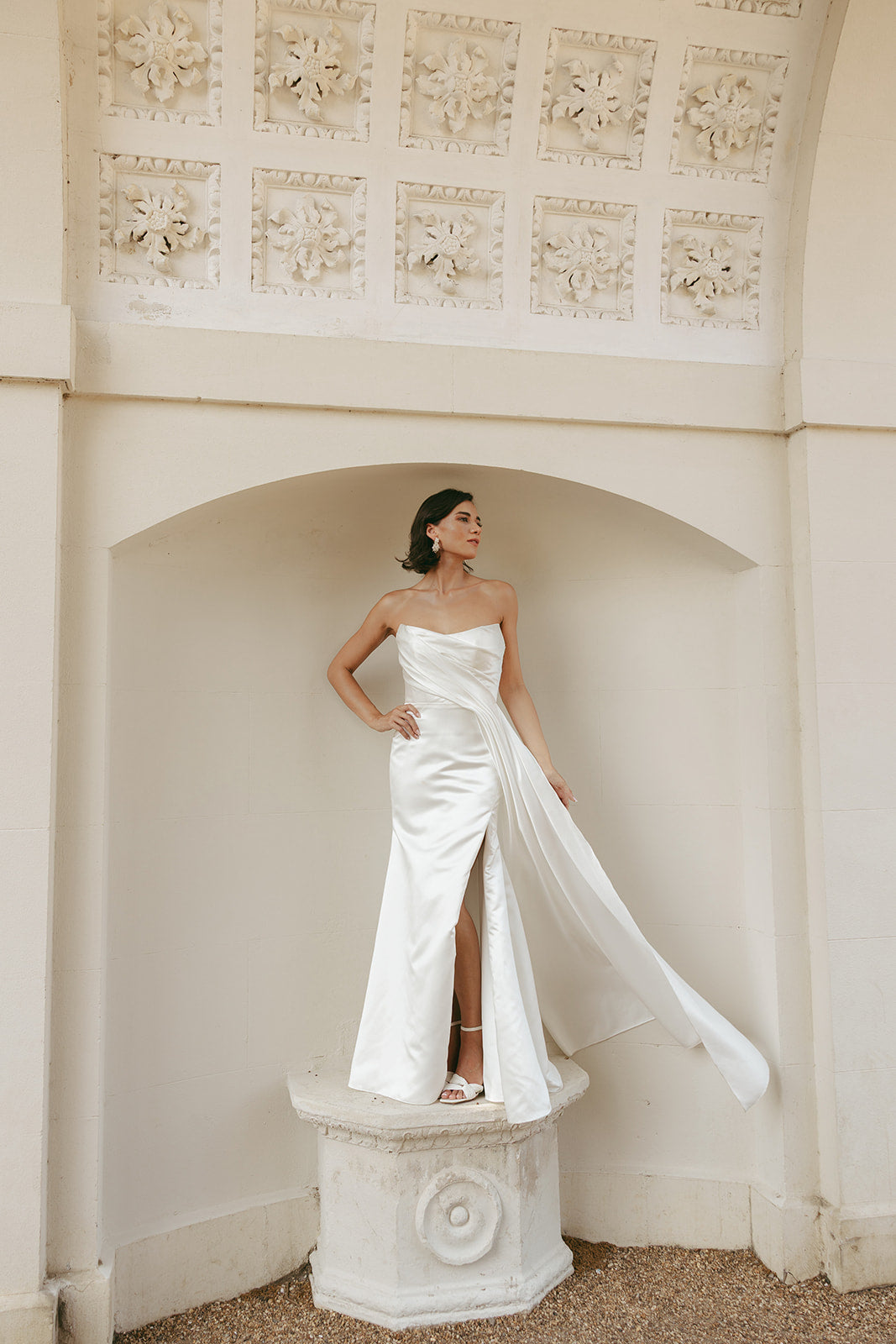 Woman in a strapless ivory wedding dress standing in an elegant architectural setting.