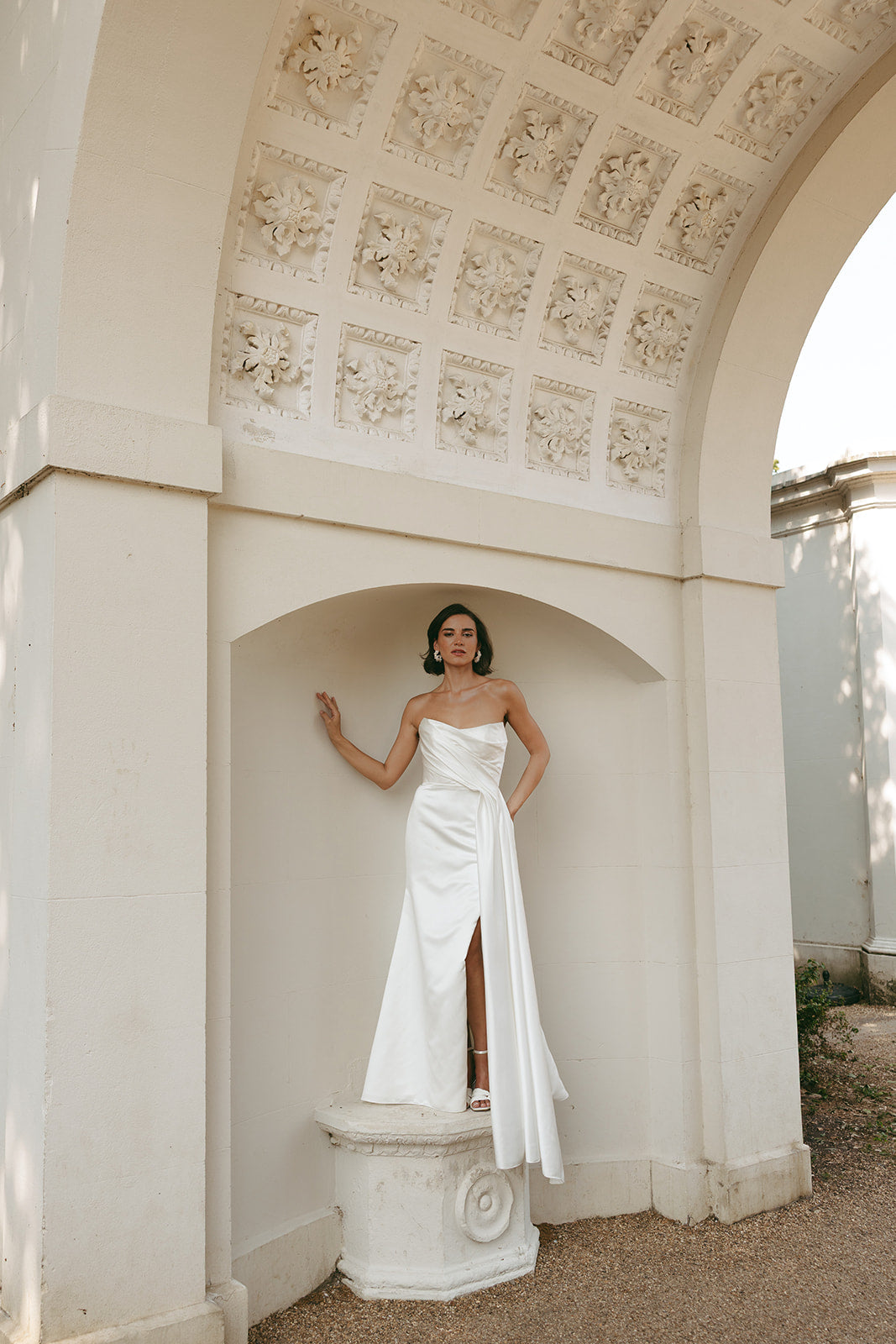 Woman in a ivory strapless satin wedding dress standing in an architectural setting with decorative columns.