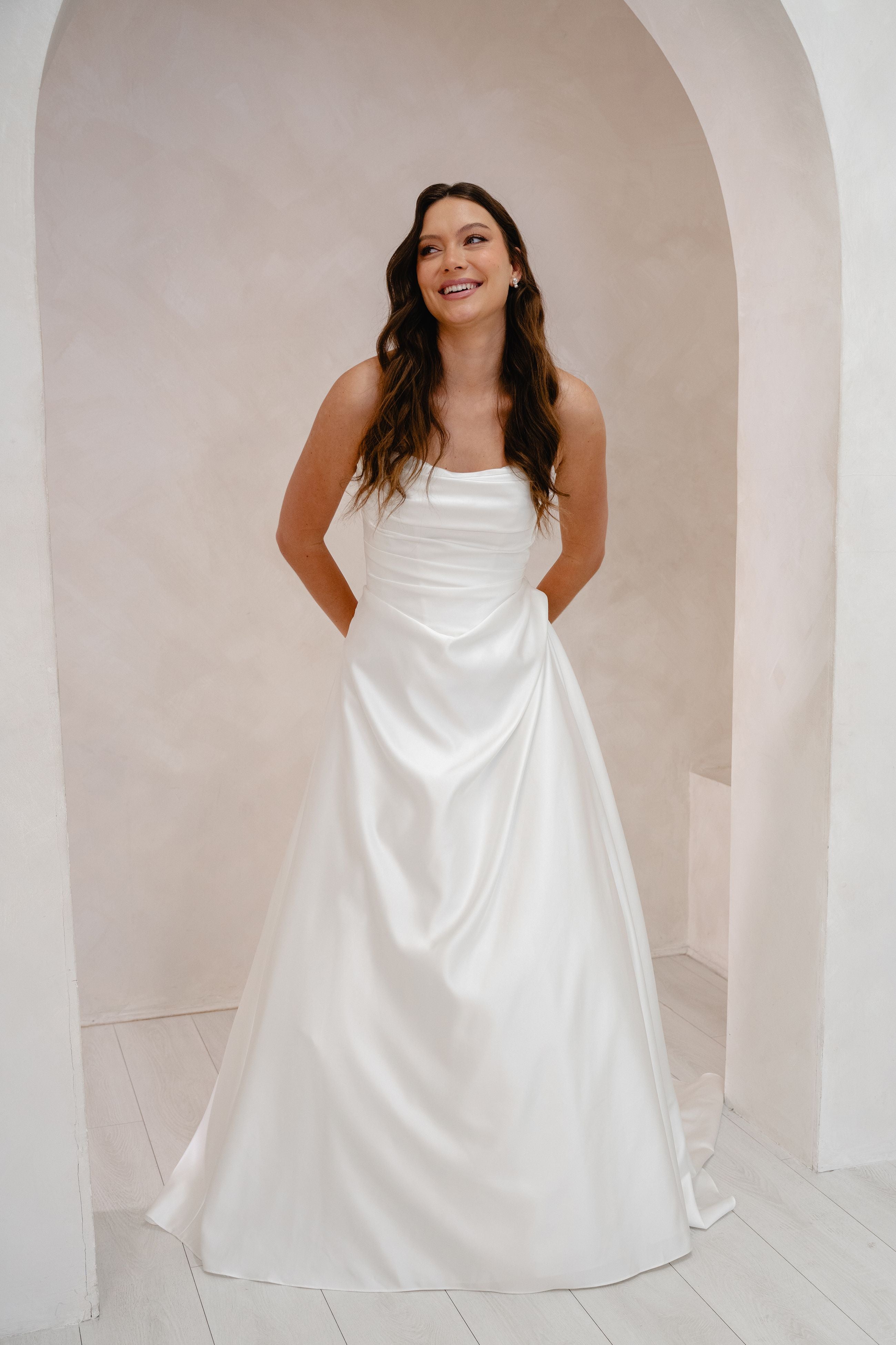 Woman wearing a white wedding dress standing in a minimalistic setting.