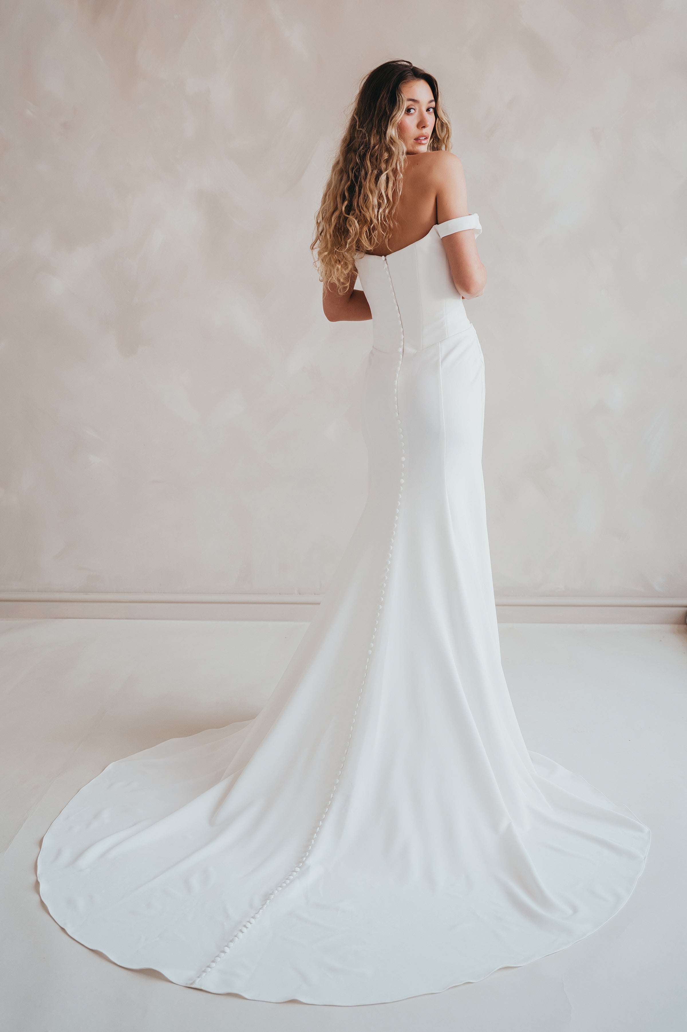 Bride wearing the Hadley off-the-shoulder stretch crepe wedding dress with draped neckline and button-back detail.