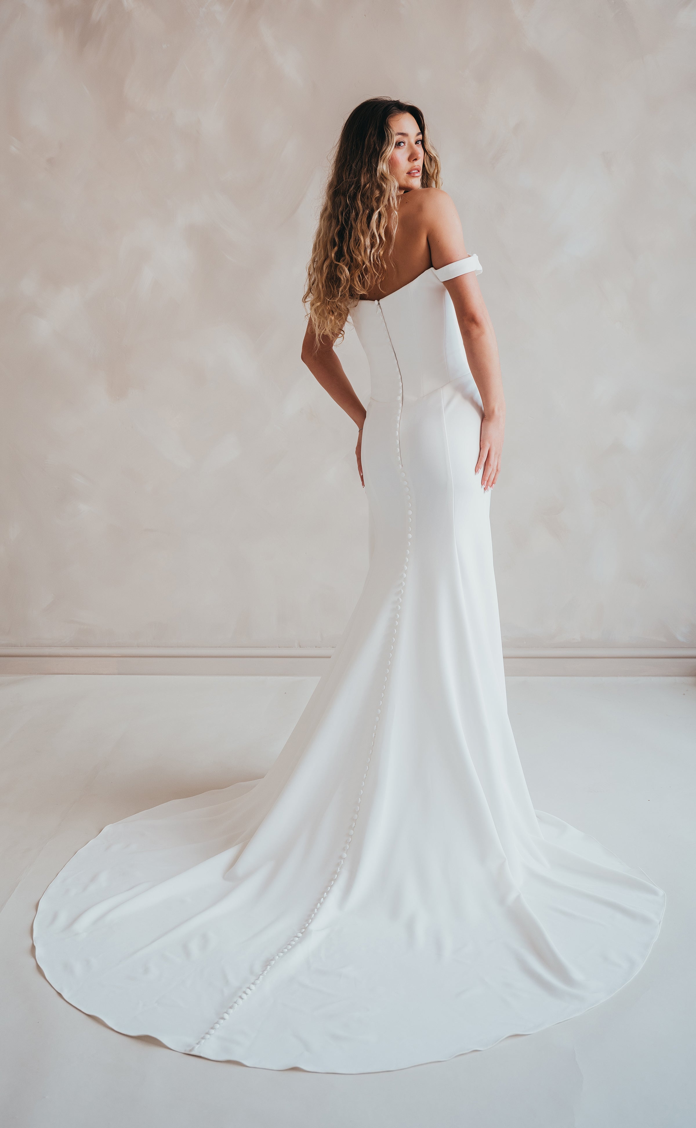 Bride wearing the Hadley off-the-shoulder stretch crepe wedding dress with draped neckline and button-back detail.
