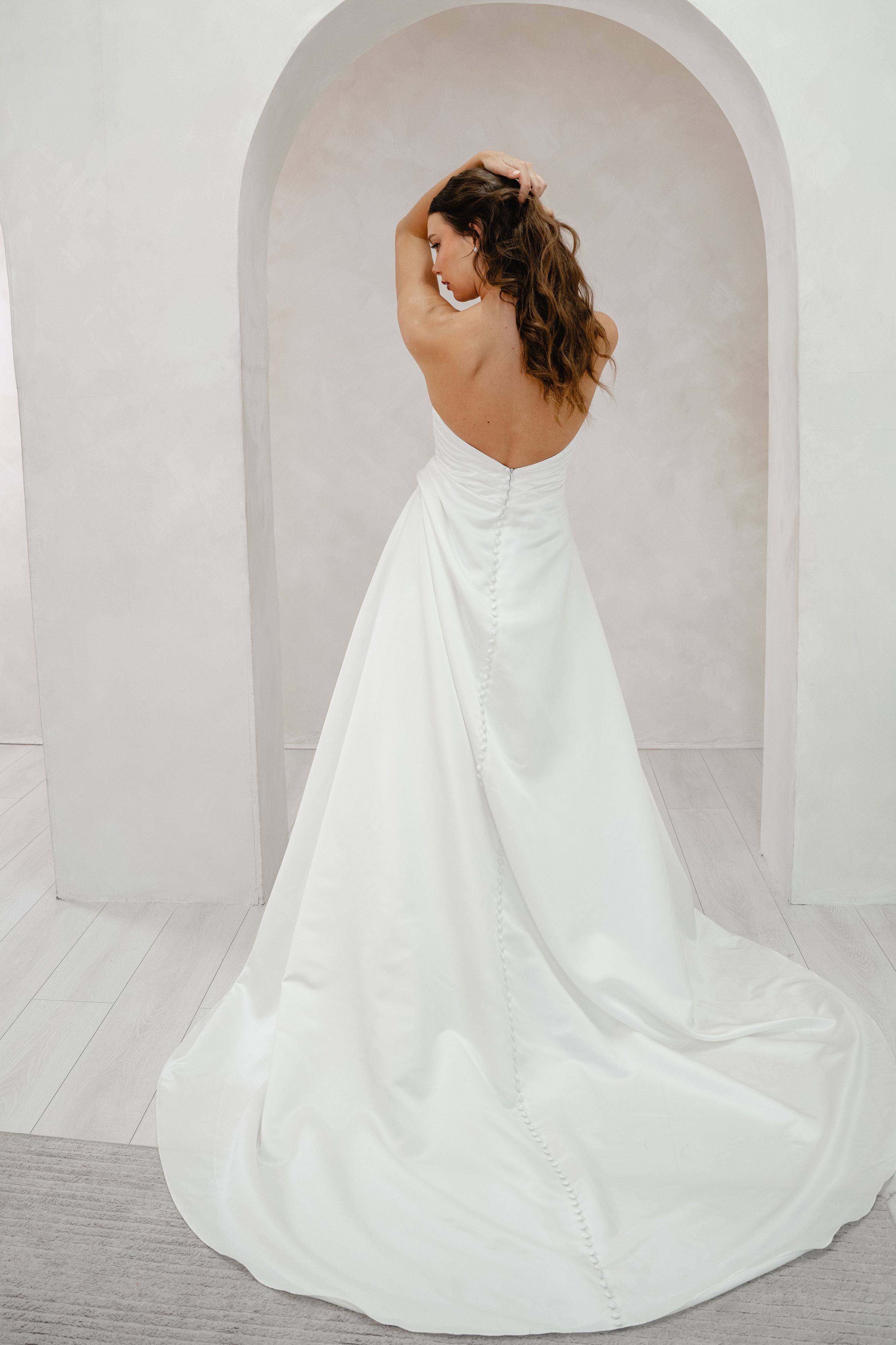 Woman in a white wedding dress standing in a minimalistic room with an archway.