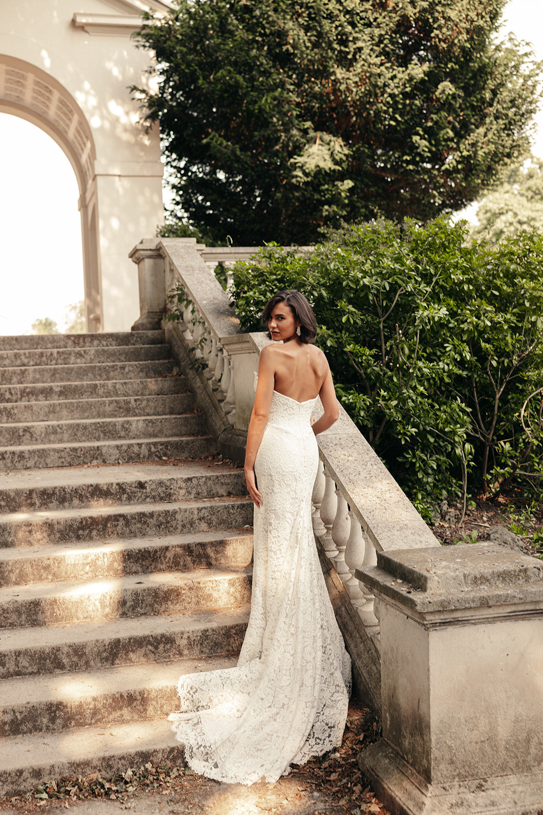 Woman in a ivory wedding dress standing on stone steps with greenery in the background