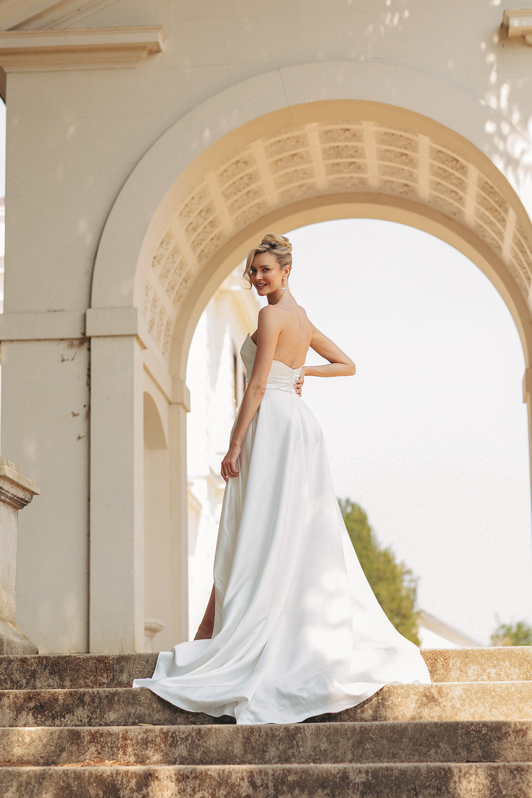 Woman in a ivory wedding dress standing under an archway with a blurred background