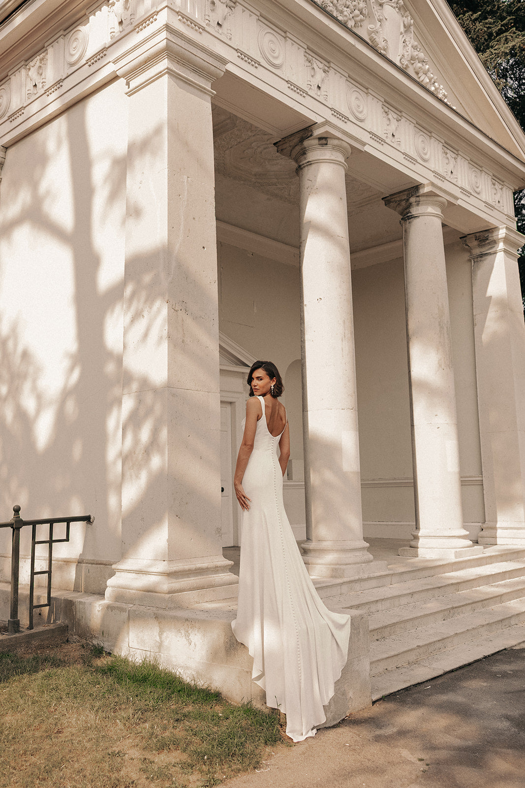 Woman in a ivory low back wedding dress standing in front of classical architecture with columns.