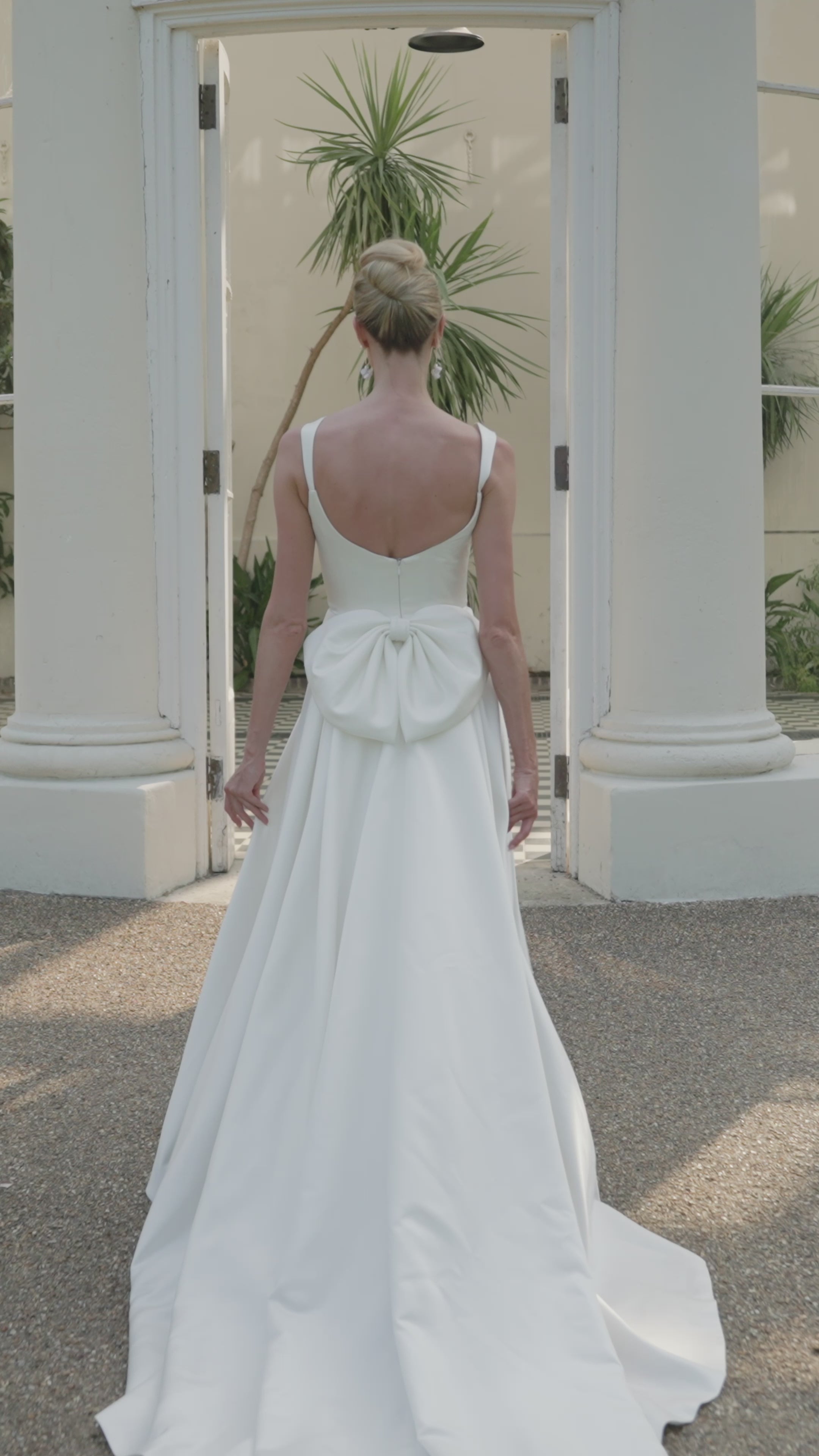 Woman in a ivory low back wedding dress moving in a conservatory.