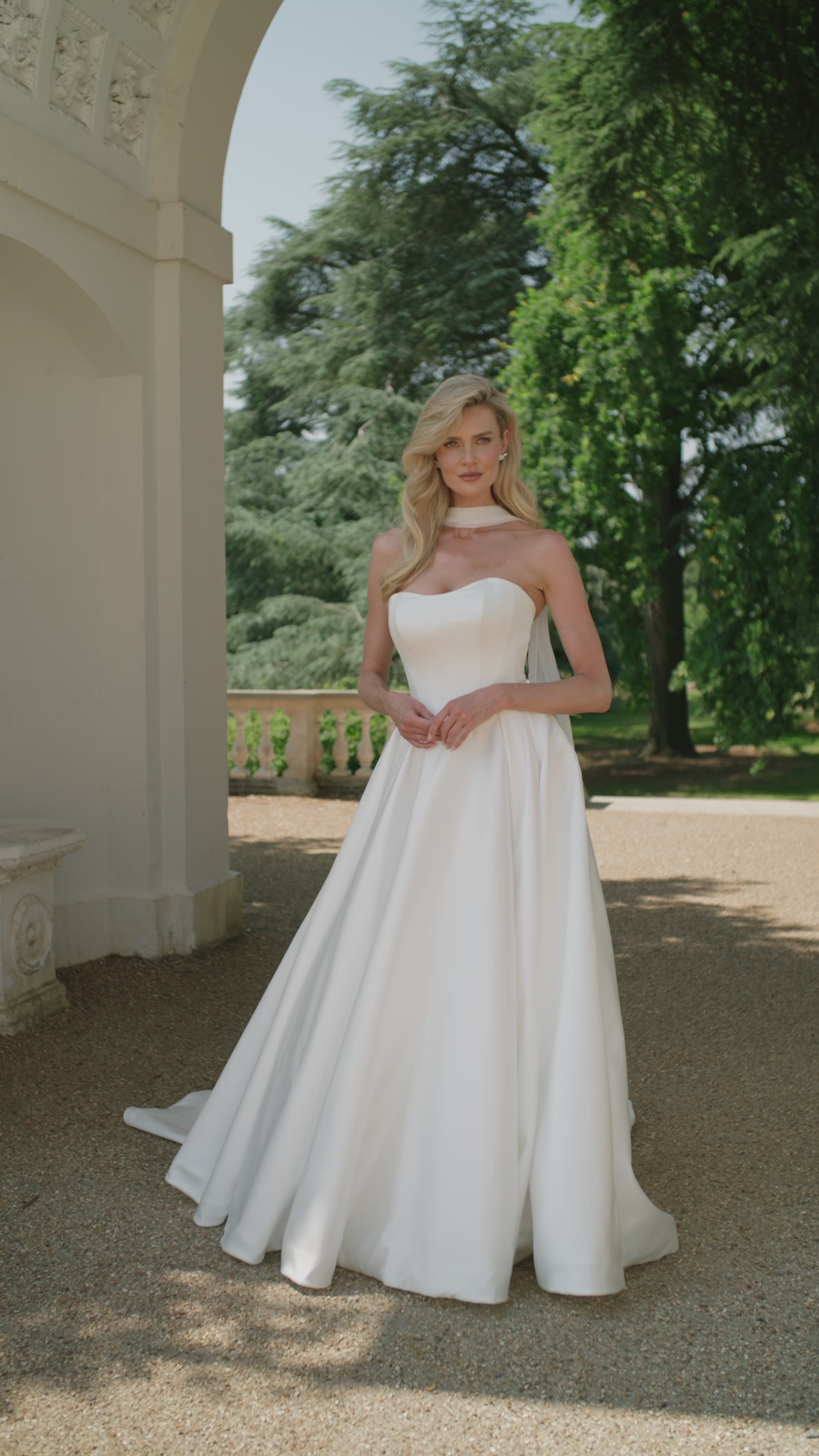 Woman in a ivory satin wedding dress moving outdoors with greenery in the background
