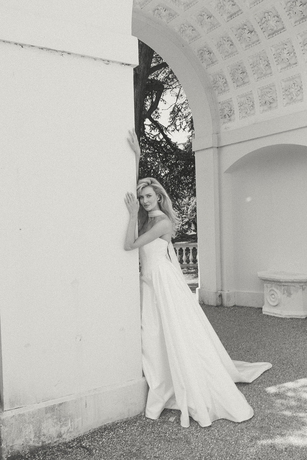 Woman in a ivory dropped waist wedding dress standing in an elegant outdoor setting with classical architecture.