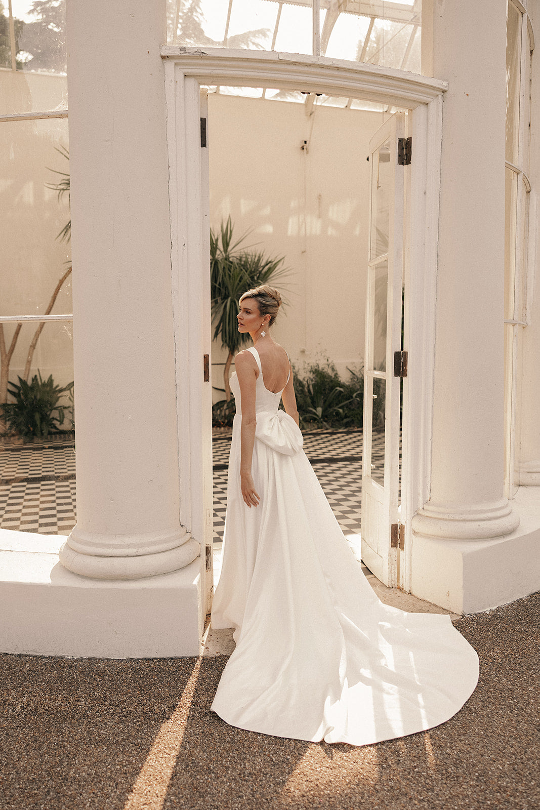 Woman in a ivory low back wedding dress standing in a conservatory.