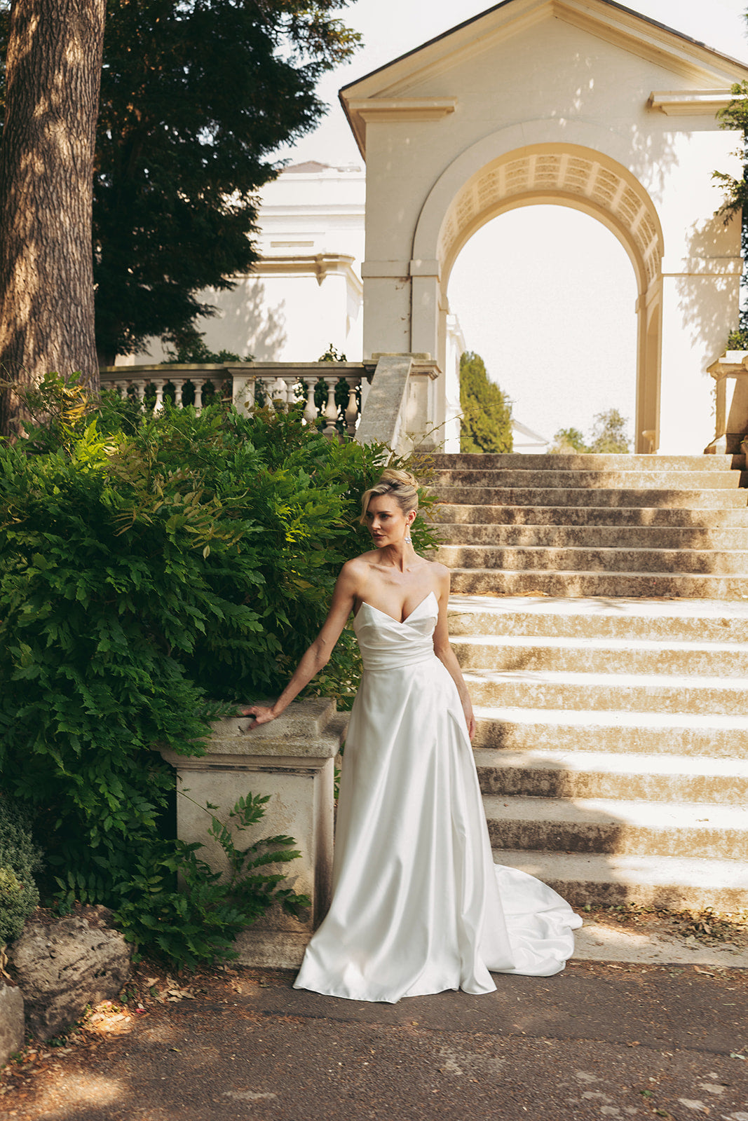 Woman in a ivory satin dress standing on stone steps with classical architecture in the background