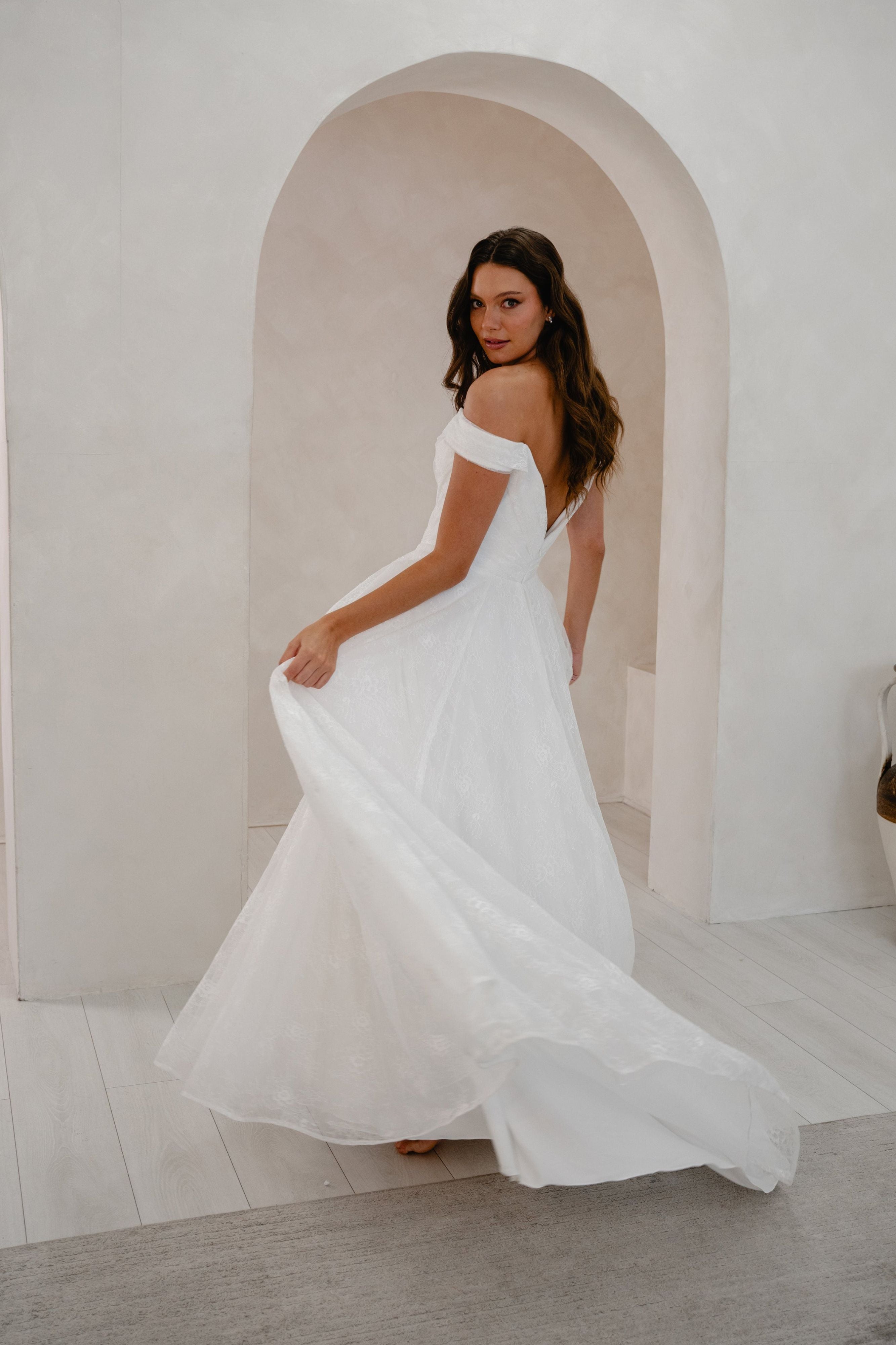 Woman in a white off-shoulder dress standing in a minimalistic room with arches.