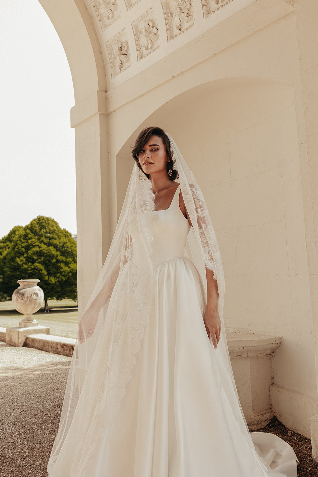 Woman in a ivory satin wedding dress with a veil standing in front of a classical building.