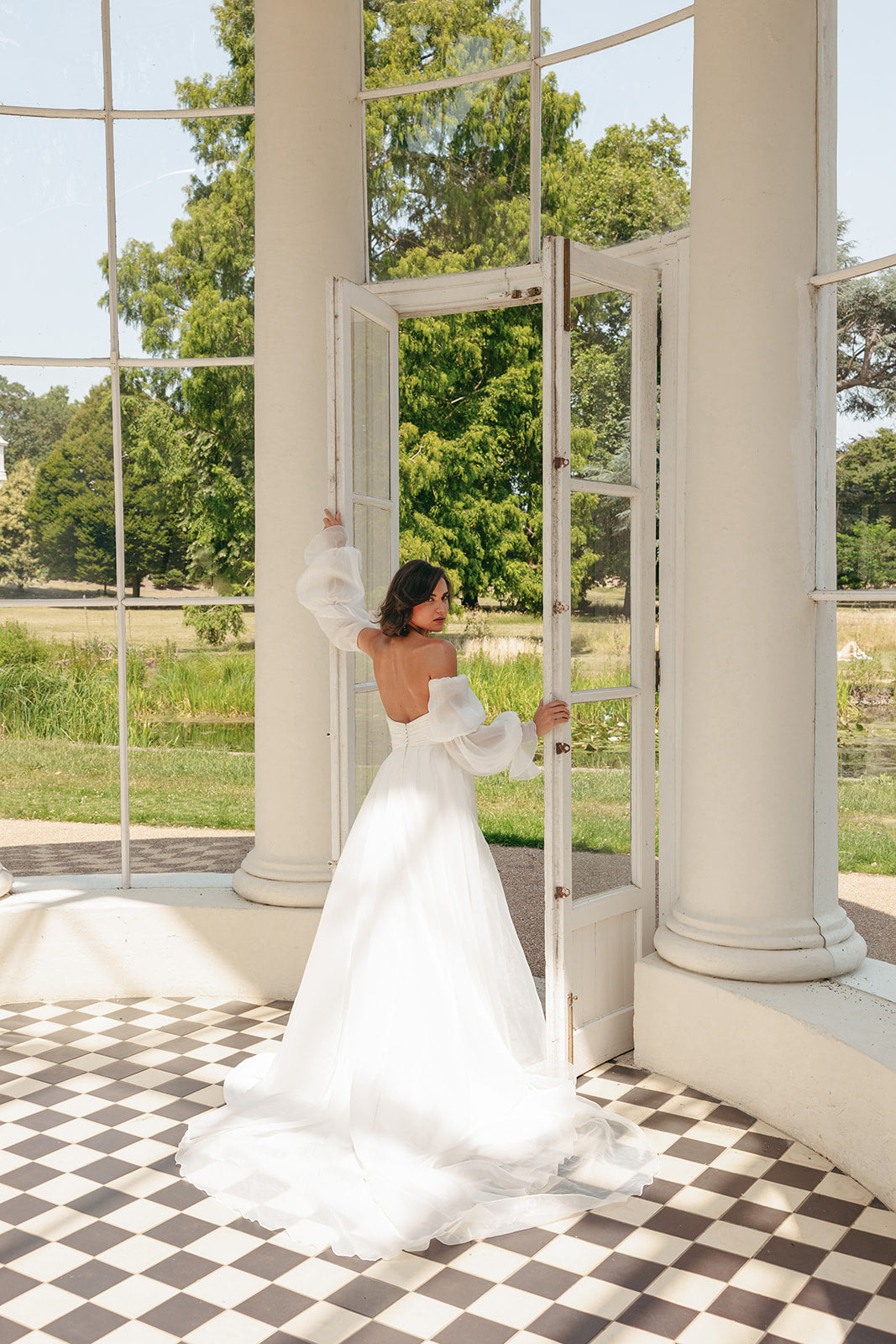 Woman in a ivory strapless wedding dress standing in a room with large windows and checkered floor.