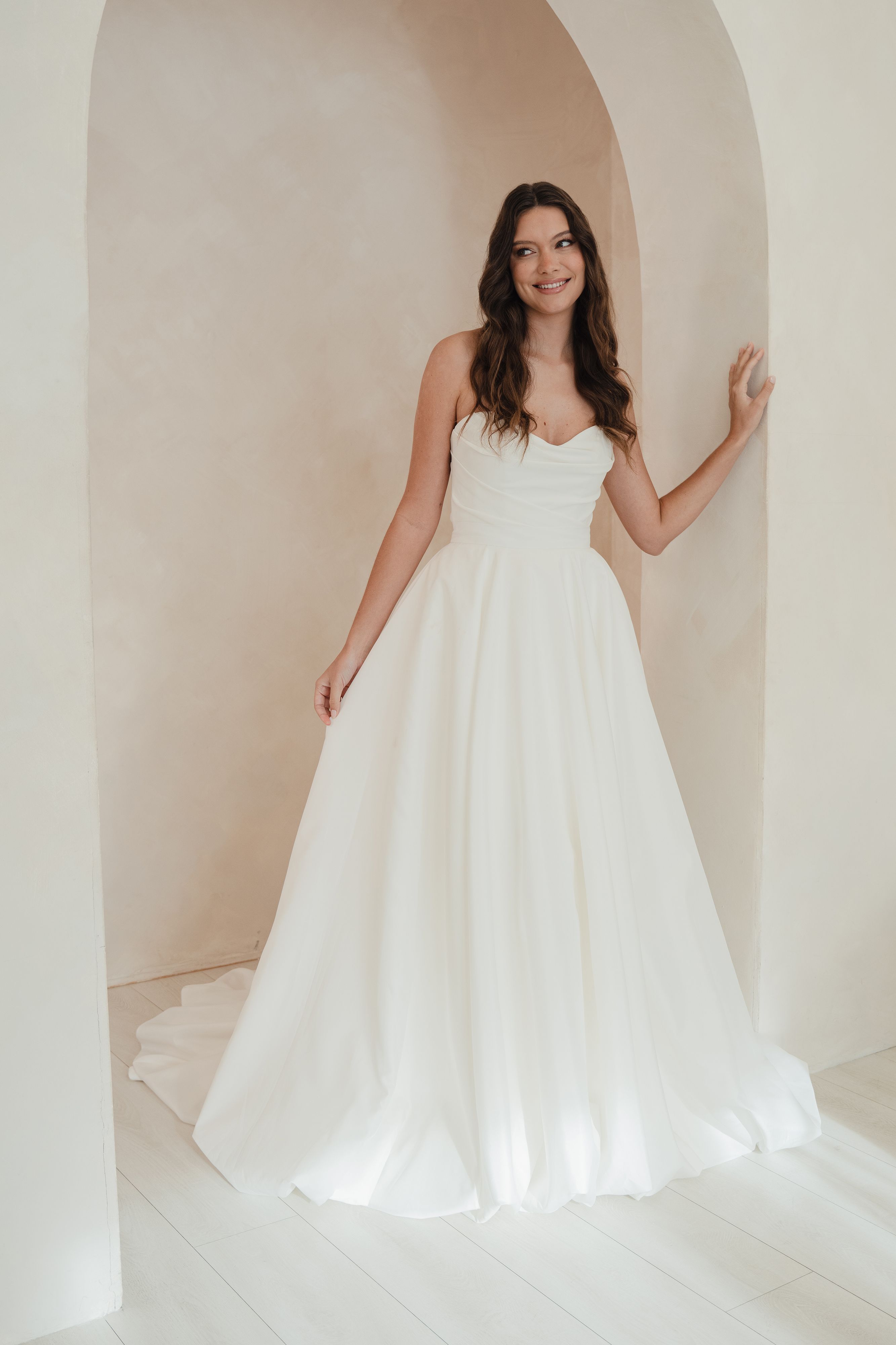 Woman in a white wedding dress standing in a softly lit room with arches.