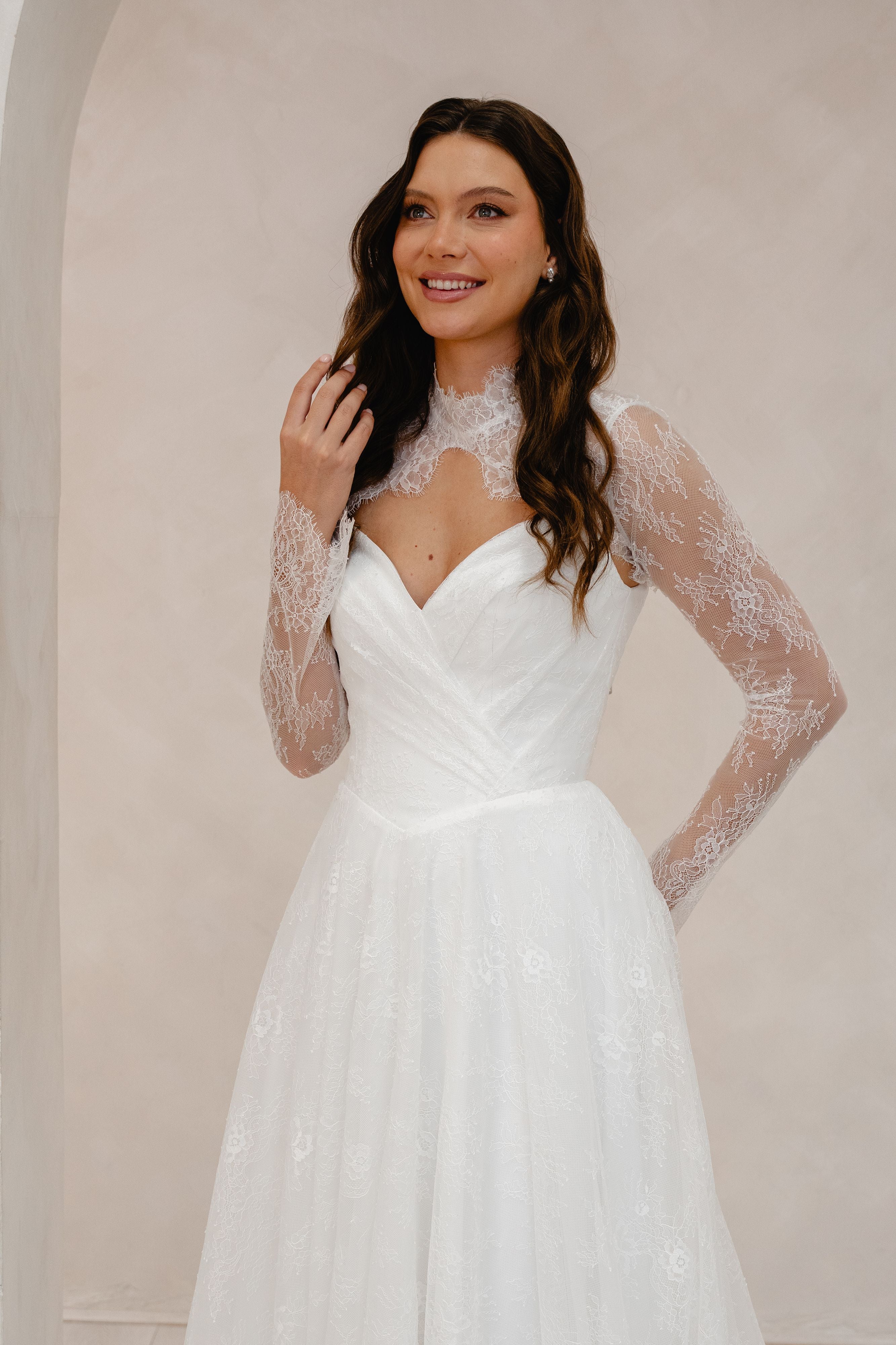 Woman wearing a white wedding dress with lace sleeves against a plain background