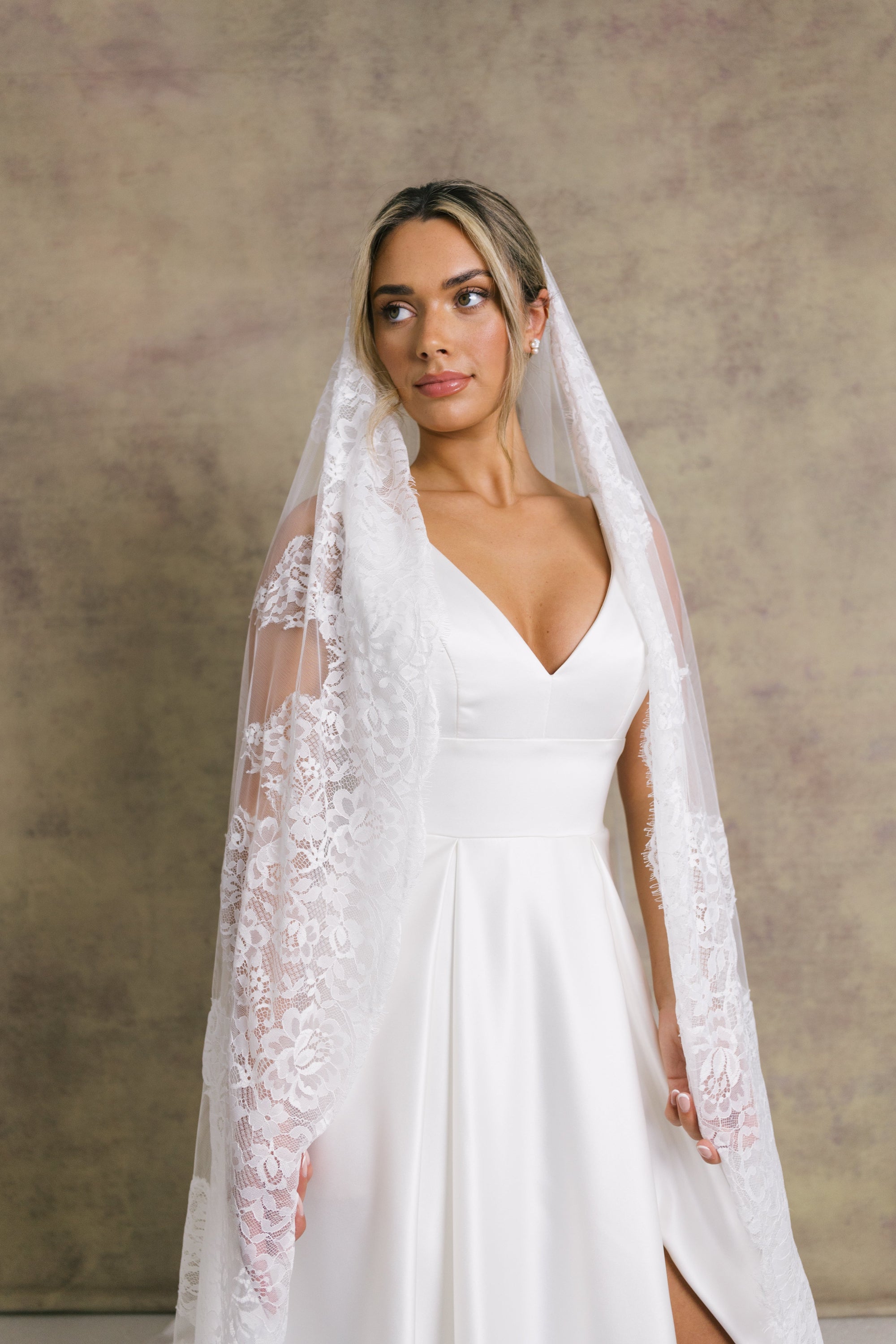 A woman wearing a beautiful chantilly lace wedding veil softly draped over the shoulders