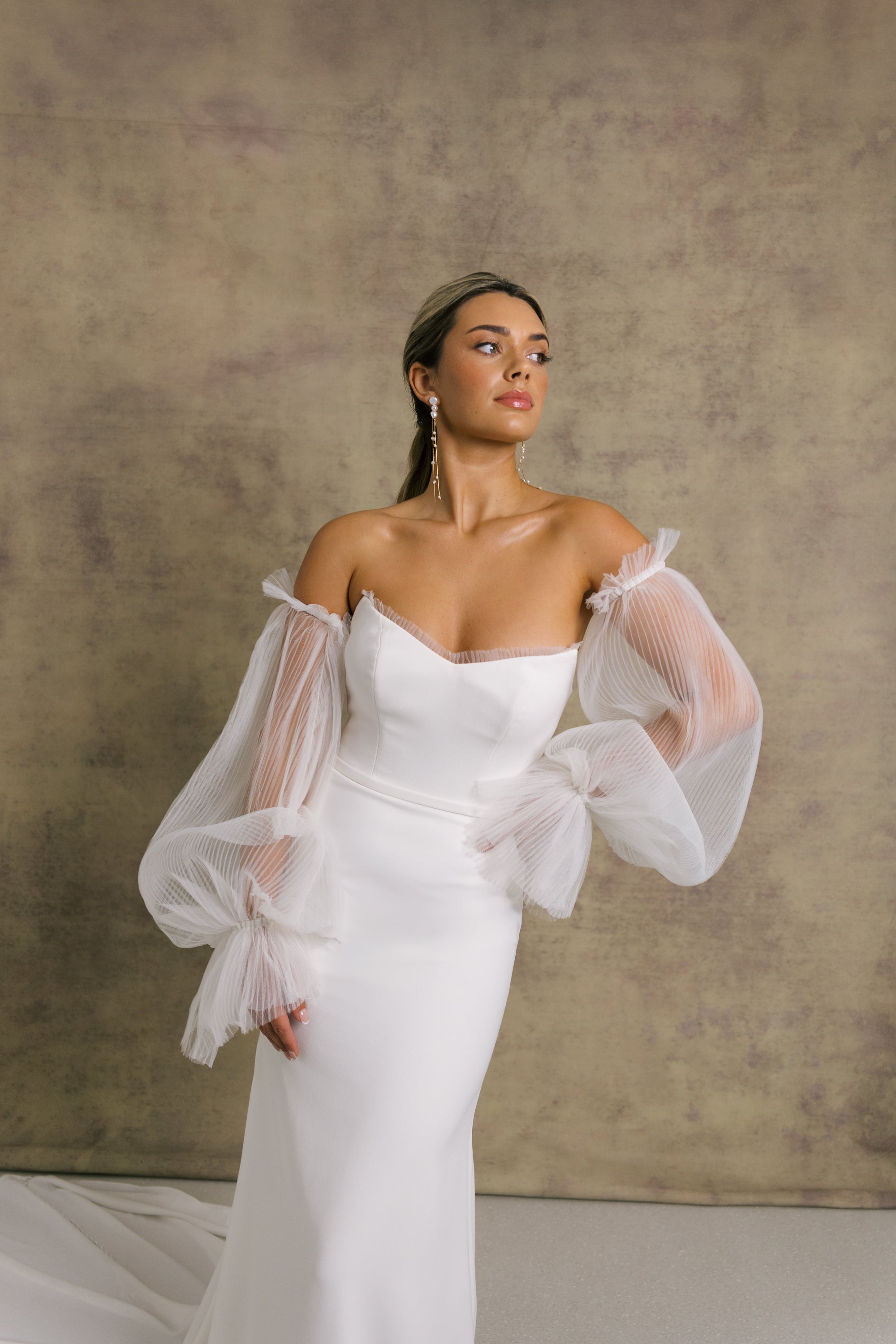 A woman in a strapless ivory wedding gown with a sweetheart neckline and sheer, pleated tulle cape showcasing the elegant fit and flare crepe skirt.