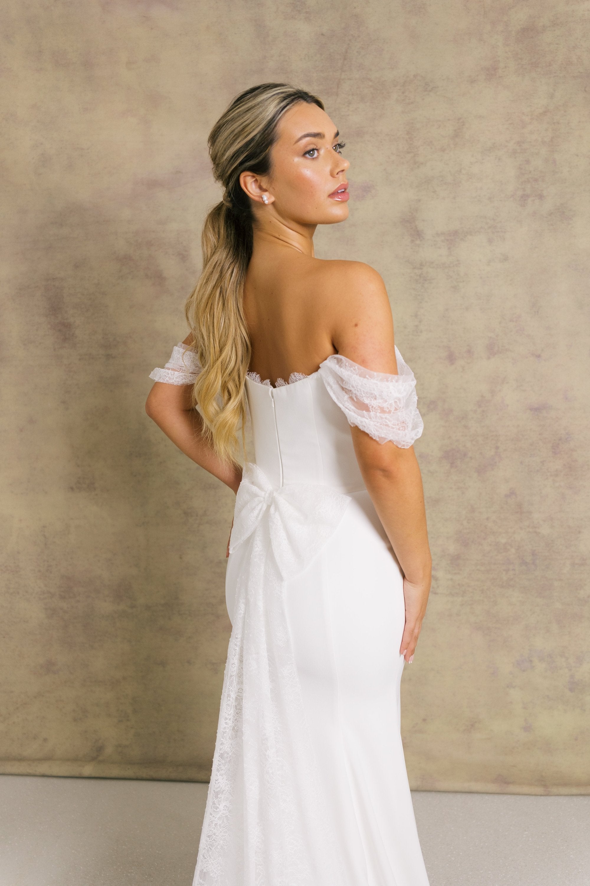 A woman in an elegant ivory strapless wedding dress with chantilly lace sleeves and a corseted bodice