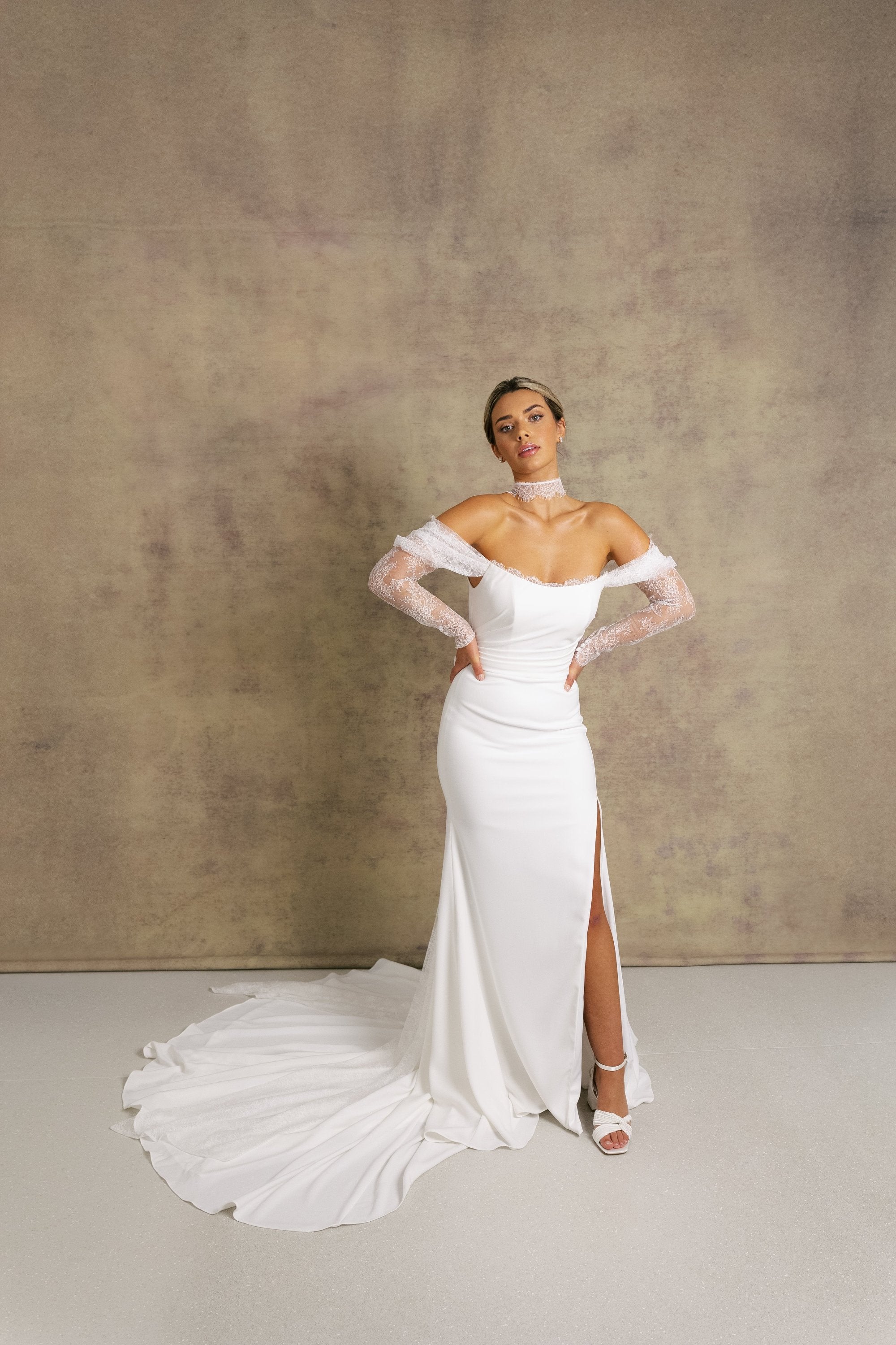 A woman in an elegant ivory strapless wedding dress with chantilly lace sleeves and a corseted bodice.