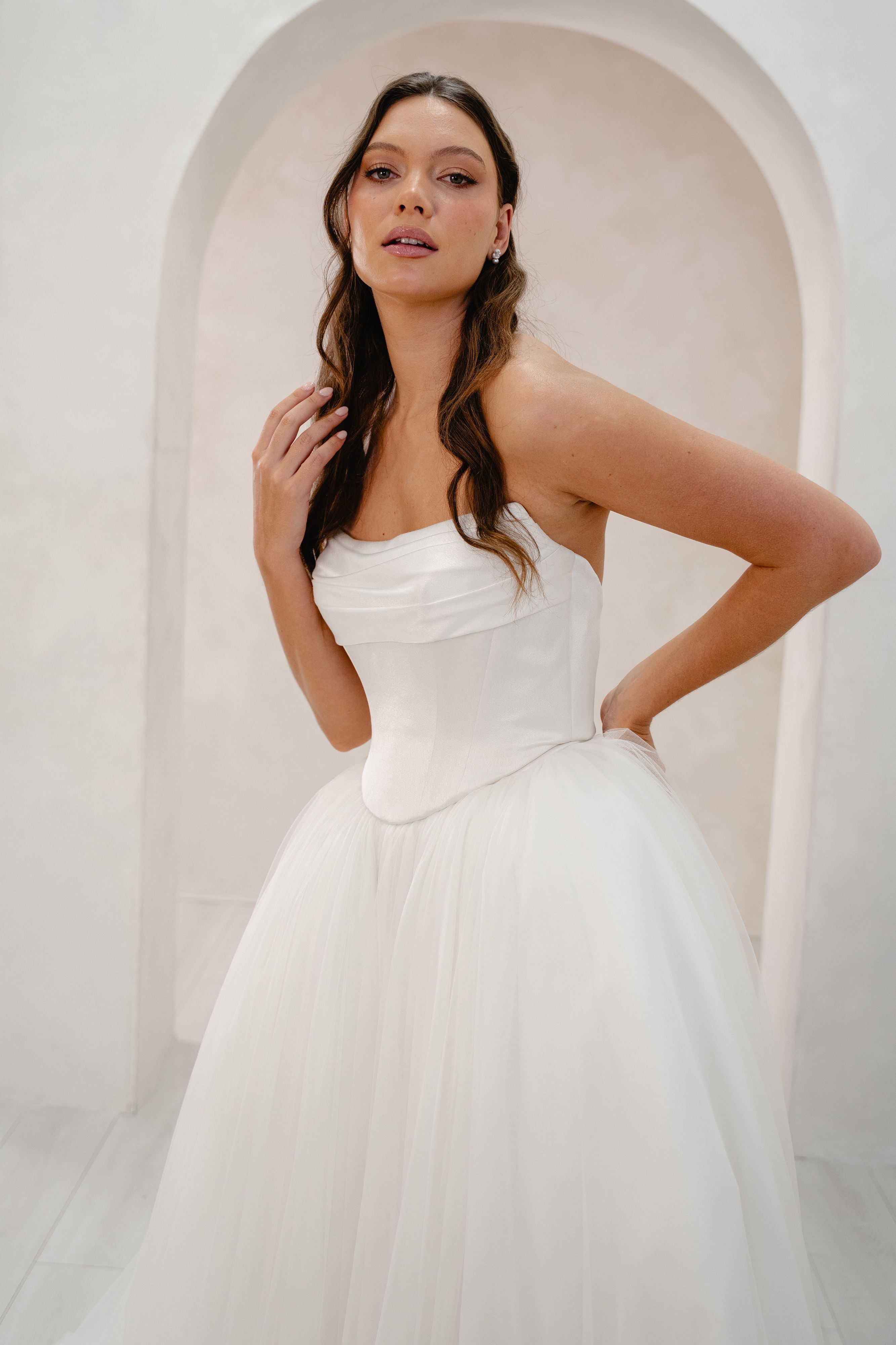 Woman in a white strapless gown standing in a softly lit room with an archway.