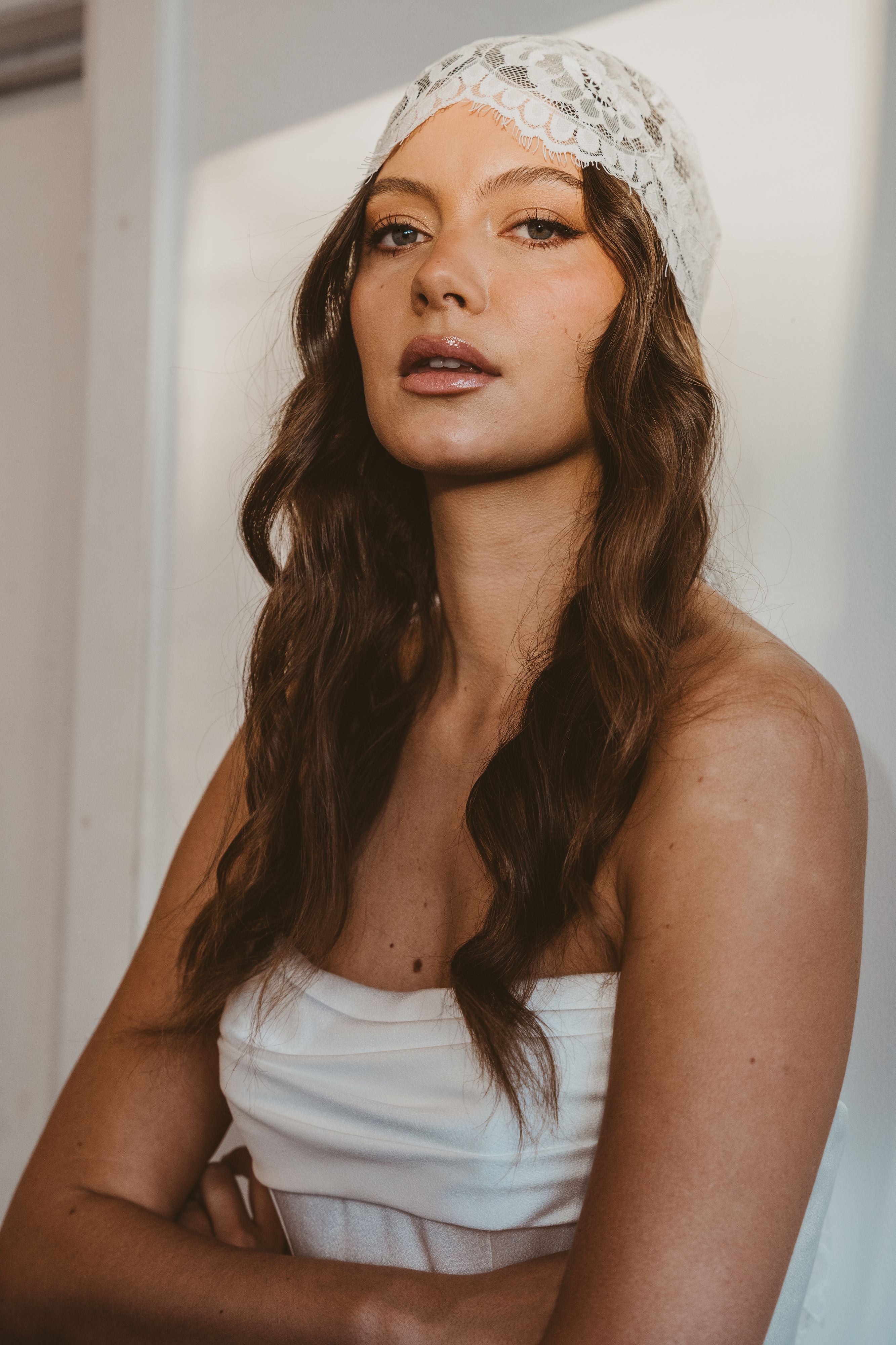 Woman wearing a white lace headband and strapless top against a neutral background