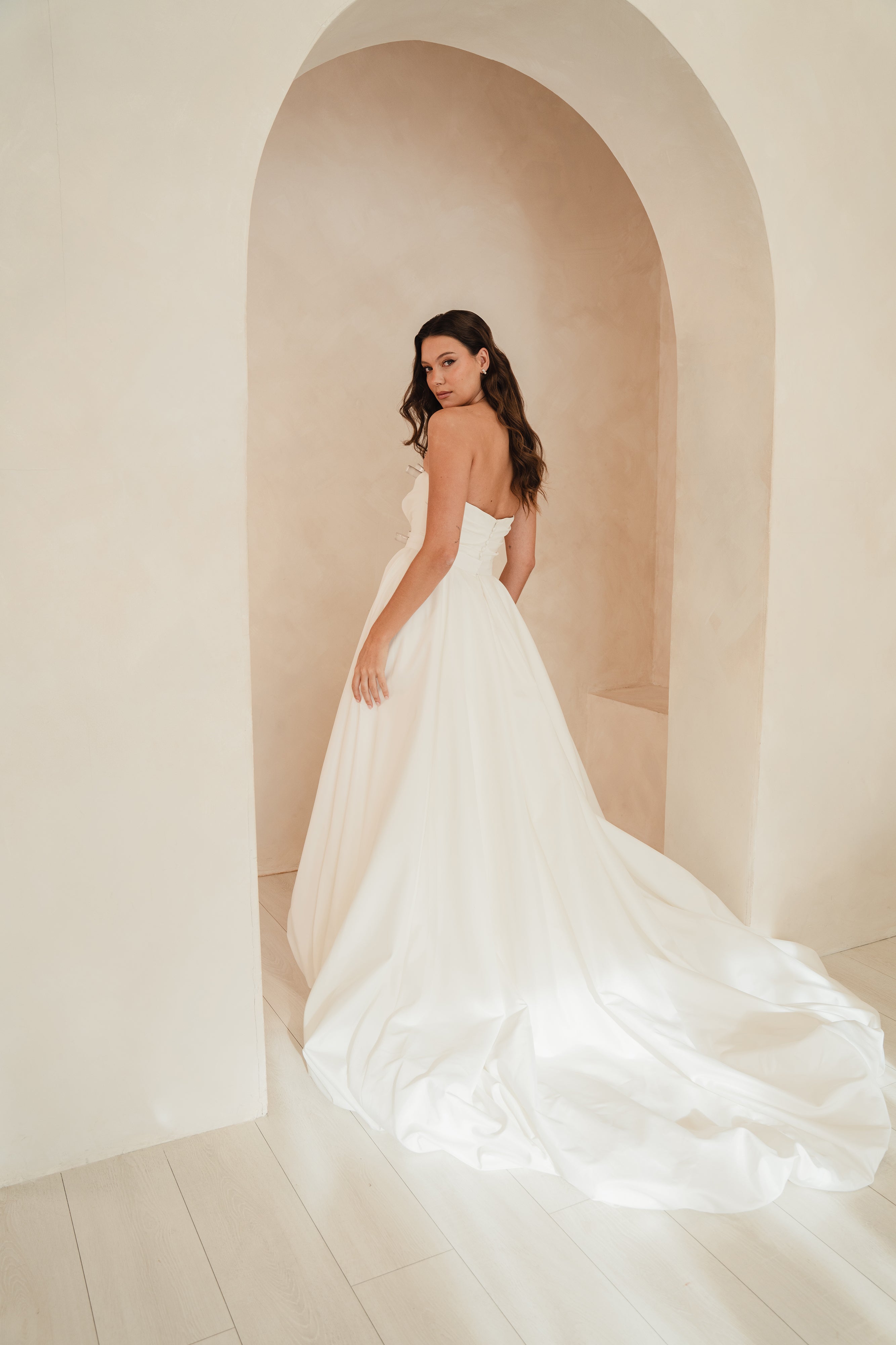 Woman in a white wedding dress standing in an archway with soft, neutral background