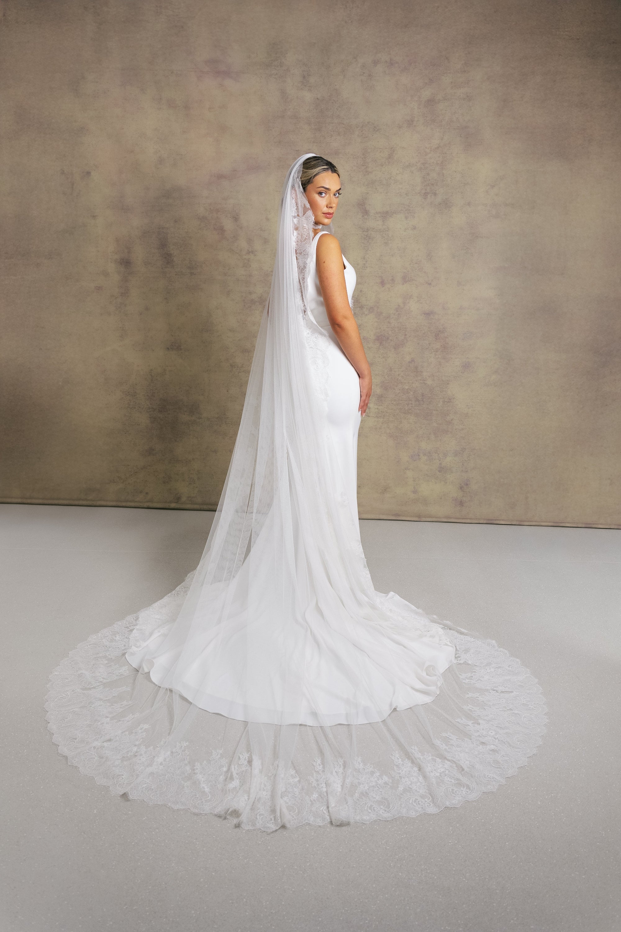 A women wearing a cathedral length Chantilly lace wedding veil with eyelash edging, beautifully framing the face and dress.