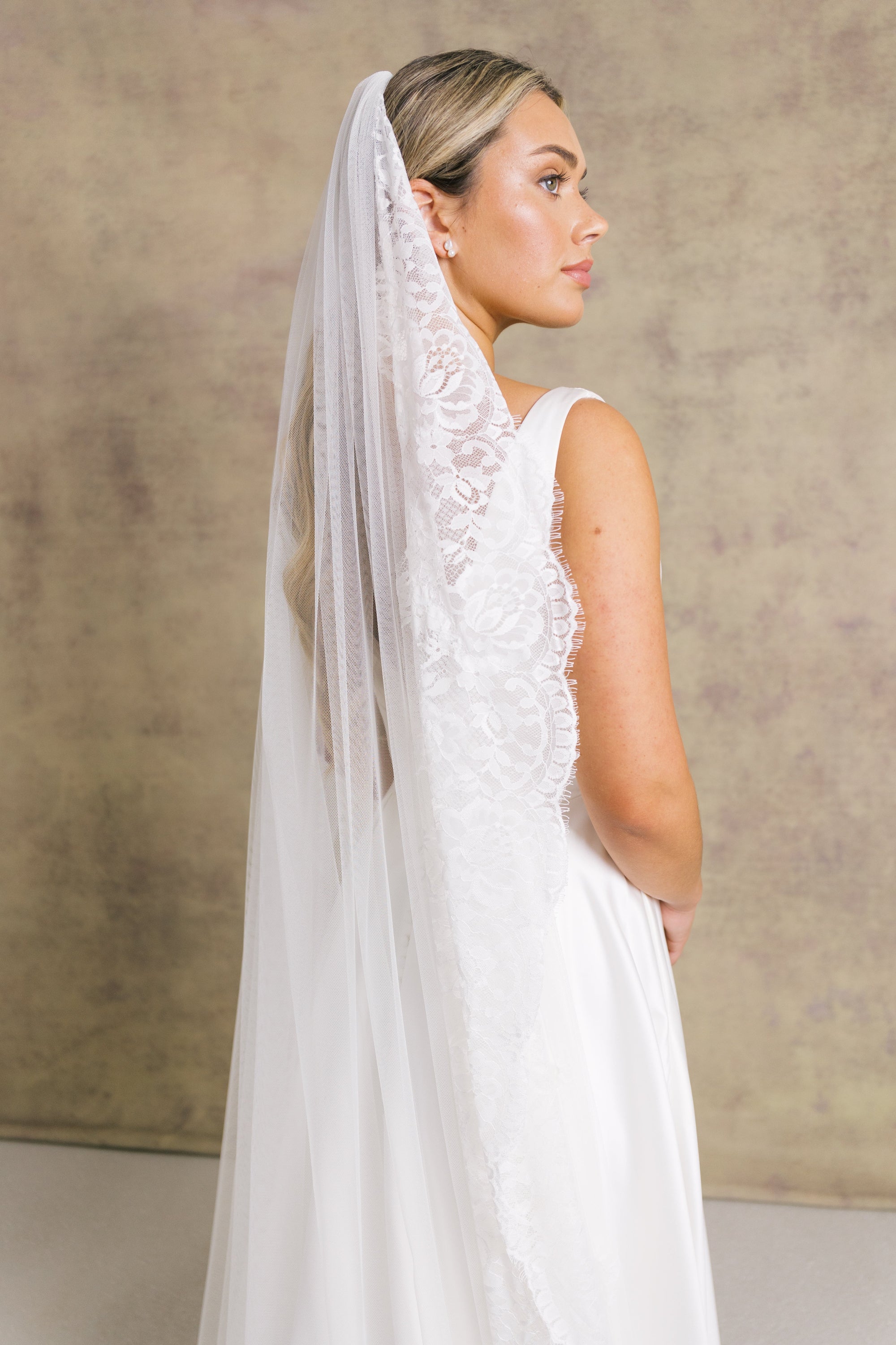 A woman wearing a lace edged chantilly lace full length bridal veil