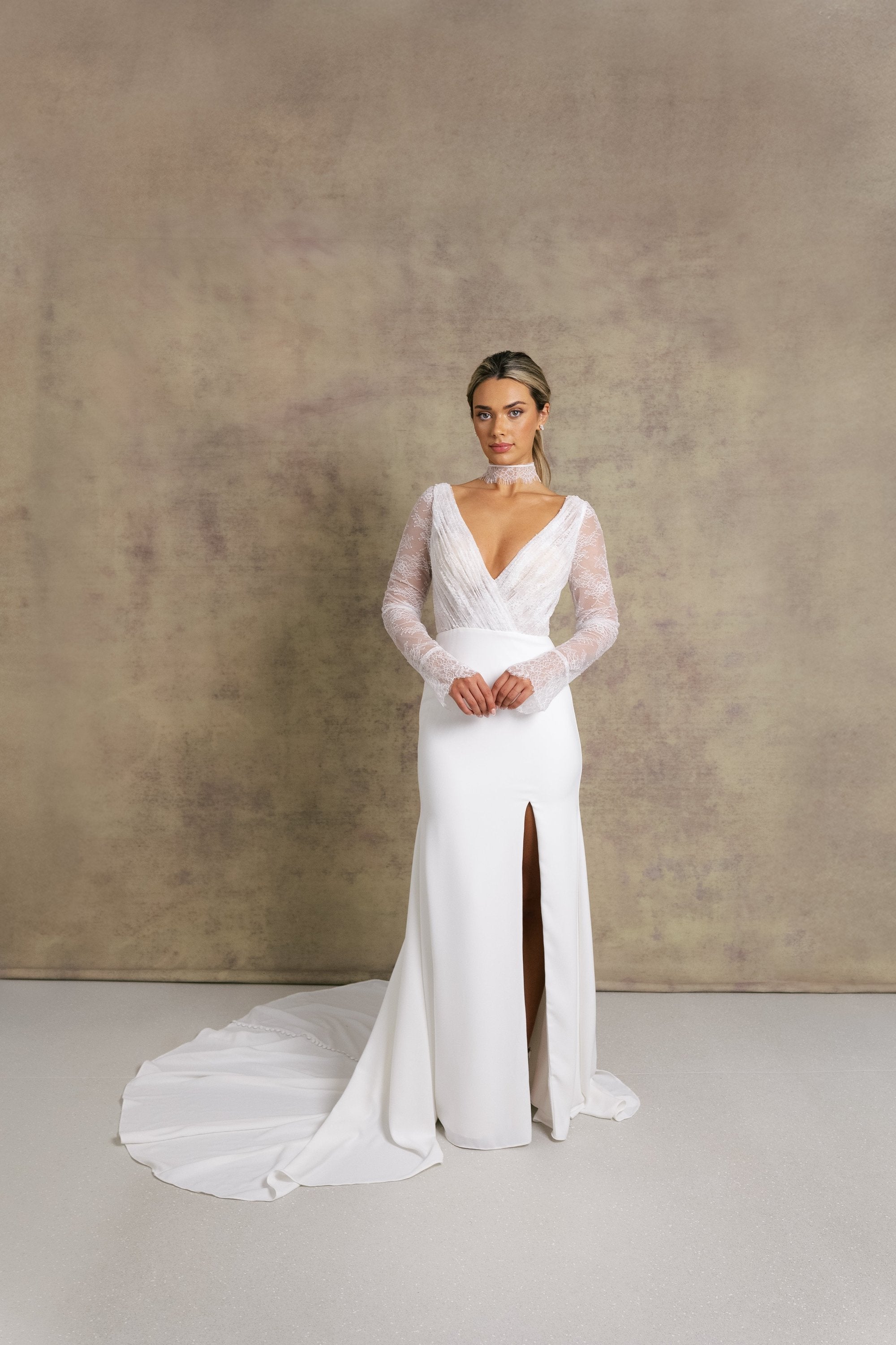 A woman in a pleated chantilly lace v neck bodice wedding dress with long sleeves, finished with dreamy, flared cuffs, complemented on fitted crepe skirt.