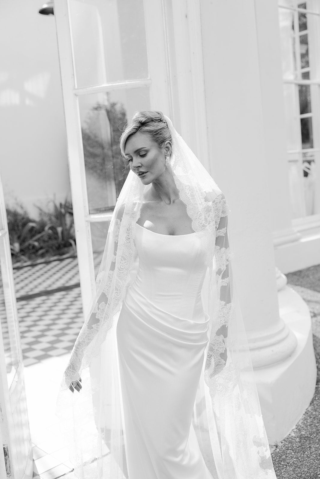 Black and white photo of a woman in a wedding dress with a veil outdoors.