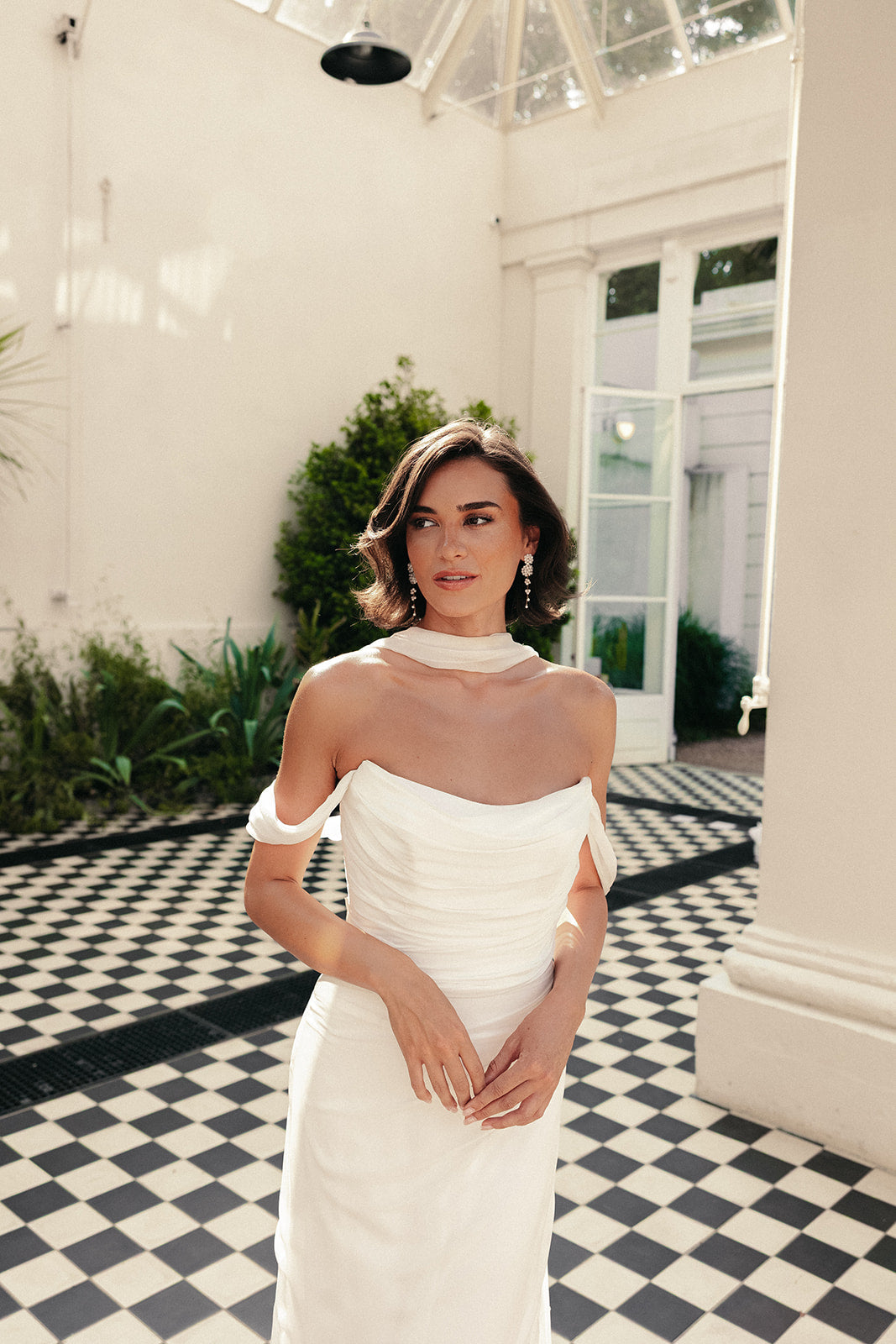 Woman in a ivory wedding dress standing in a stylish interior setting with checkered floor and columns.