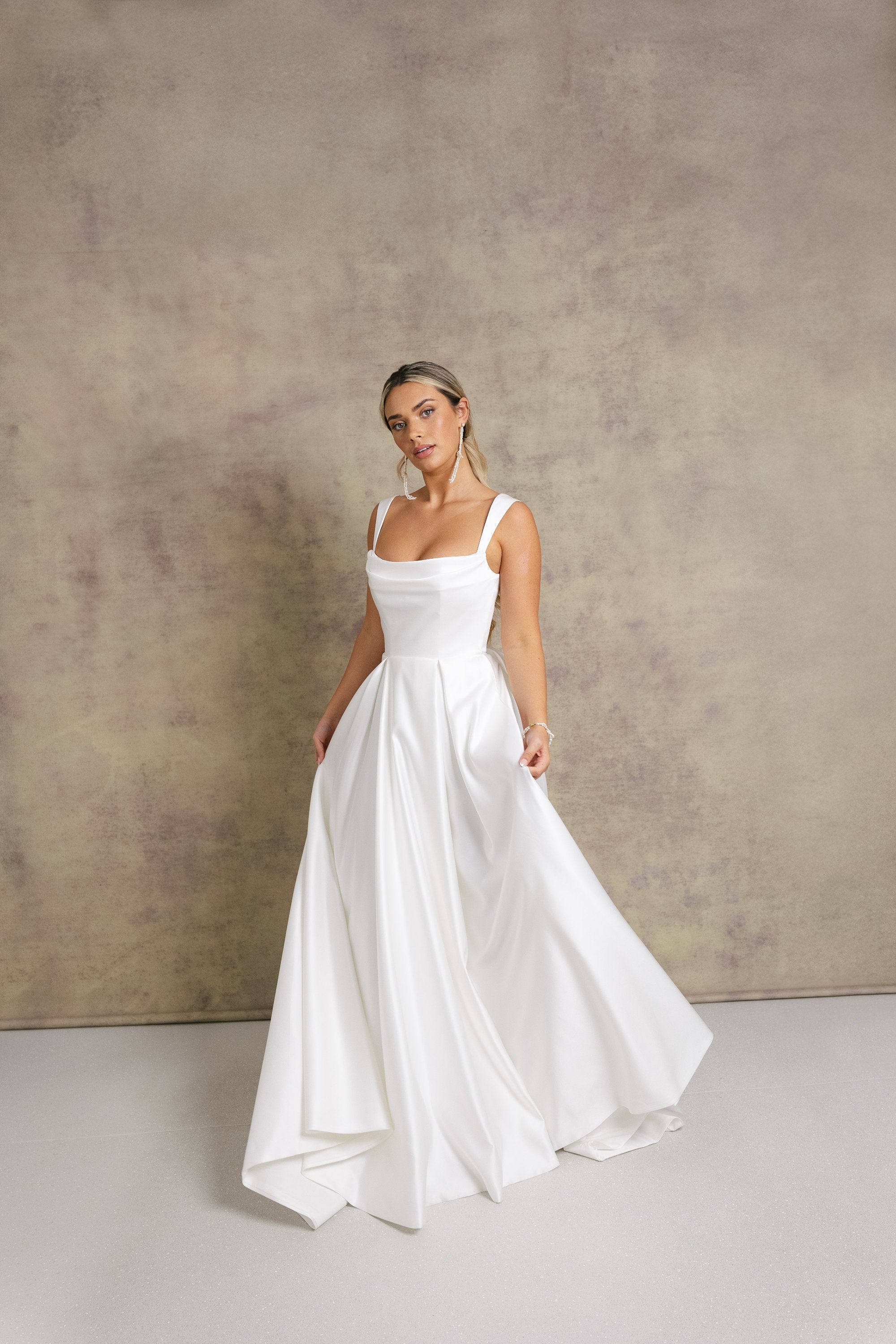 A woman in a satin striking cowl neckline wedding dress with a box pleated soft Aline skirt.