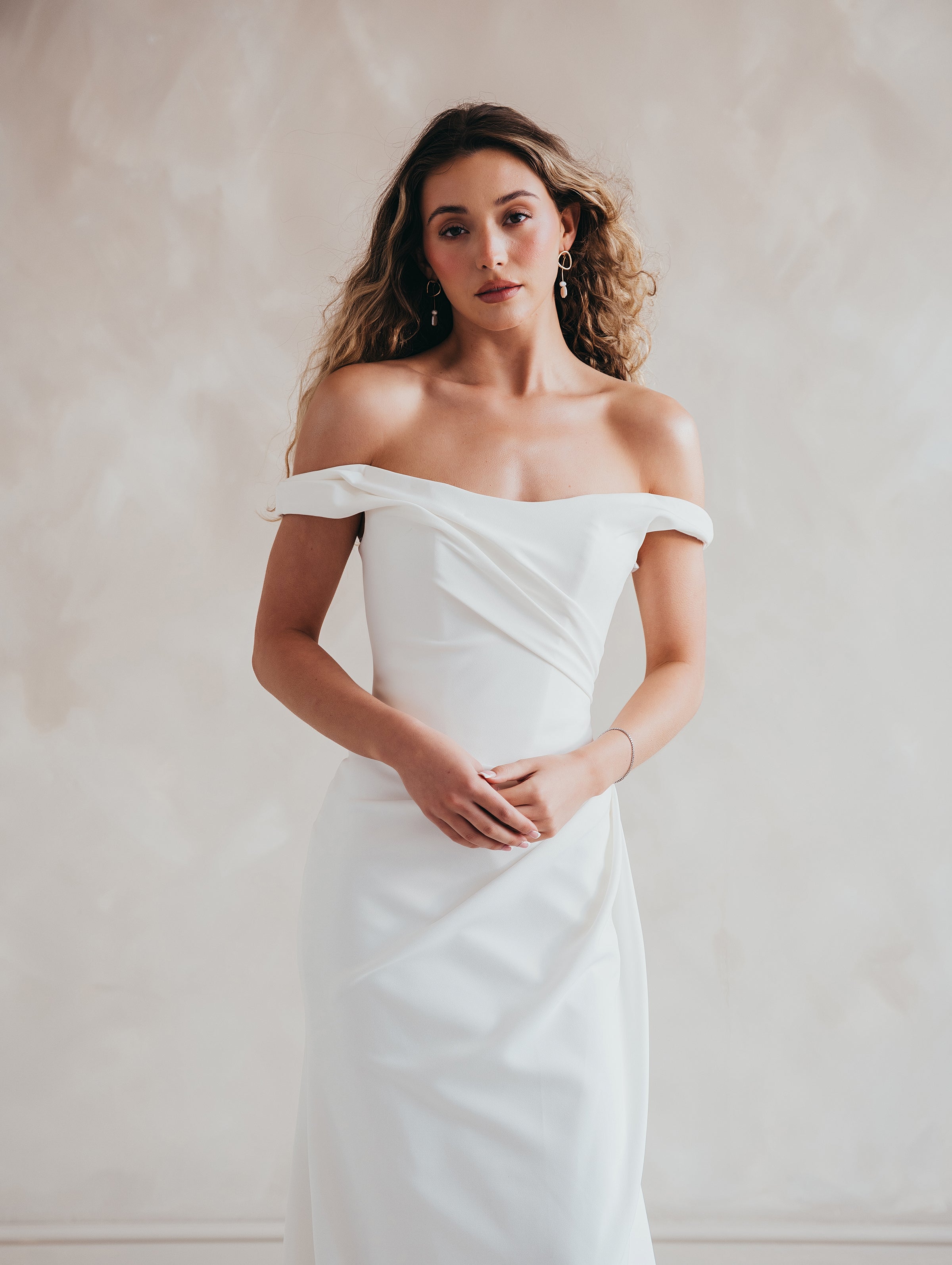 Bride wearing the Hadley off-the-shoulder stretch crepe wedding dress with draped neckline and button-back detail.