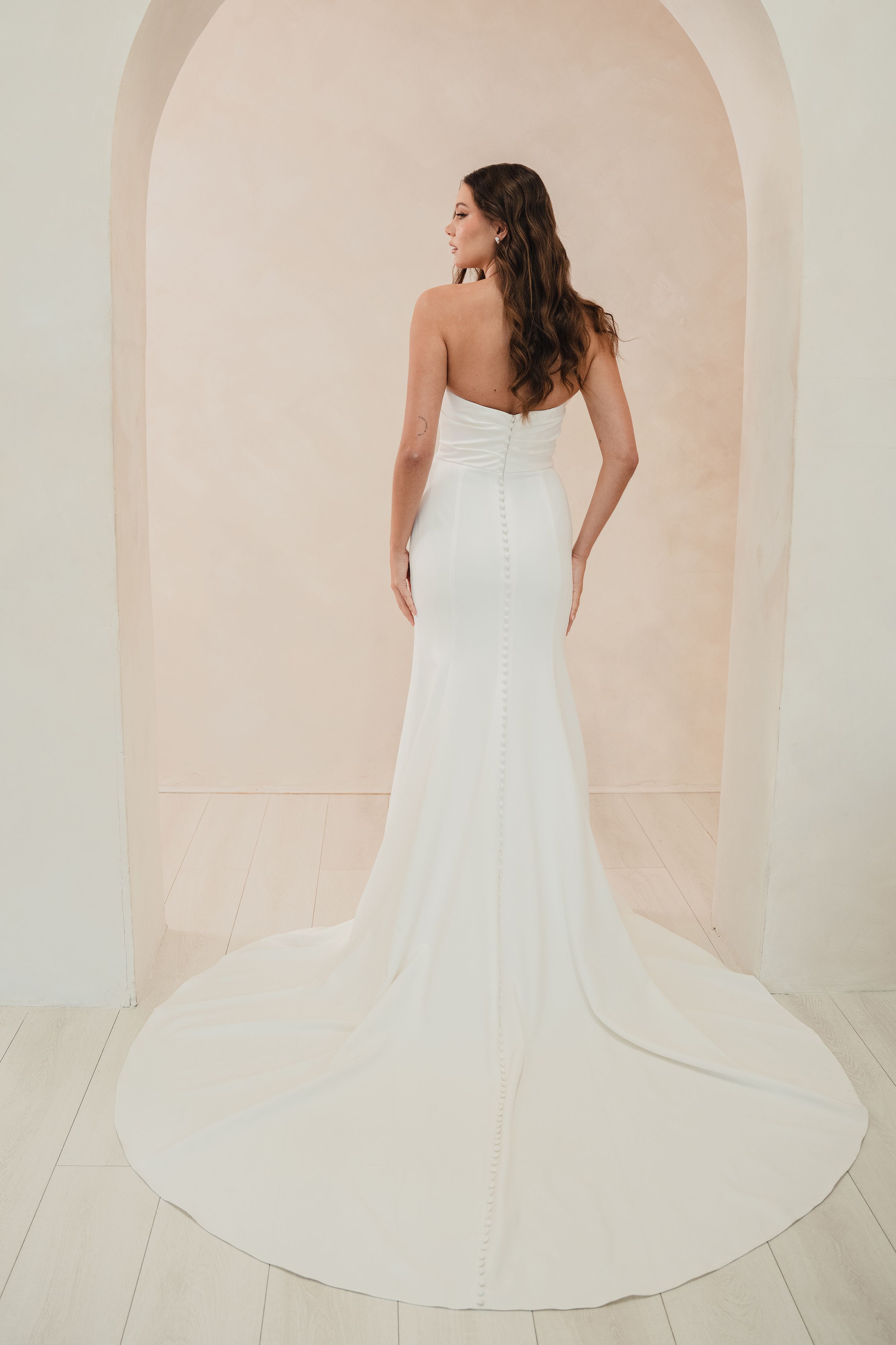 Woman in a white strapless gown standing in a softly lit room with an archway.