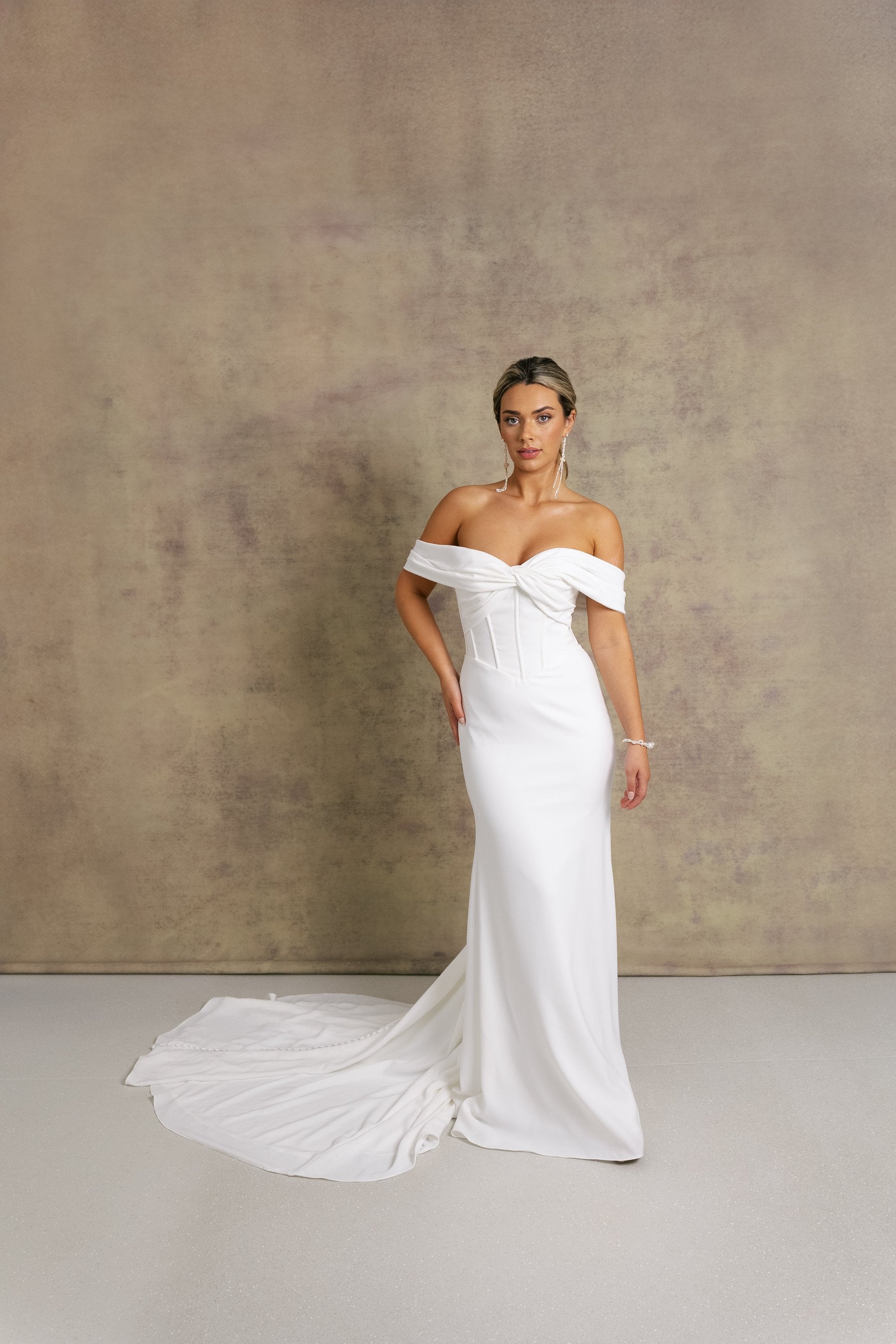 A woman in a gorgeous off shoulder sweetheart dropped waist wedding dress, featuring exposed boning on a crepe fit and flare skirt. 