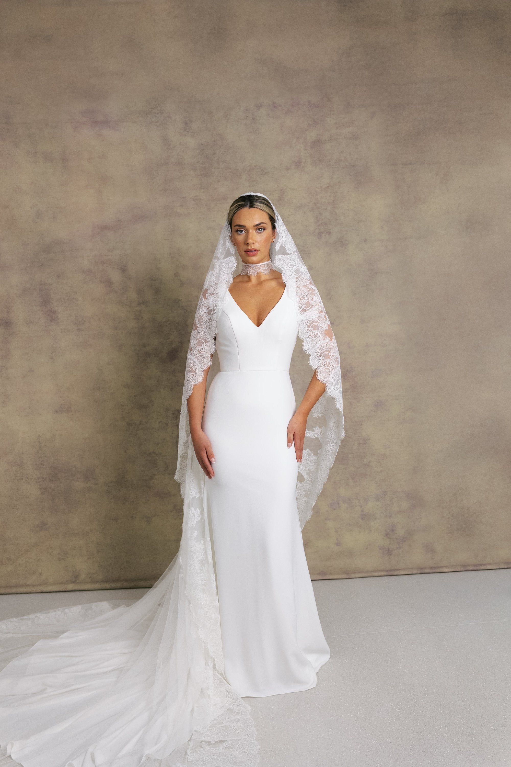 A woman in a sleek and elegant v neck fit and flare wedding dress, styled with Chantilly lace necktie and veil.