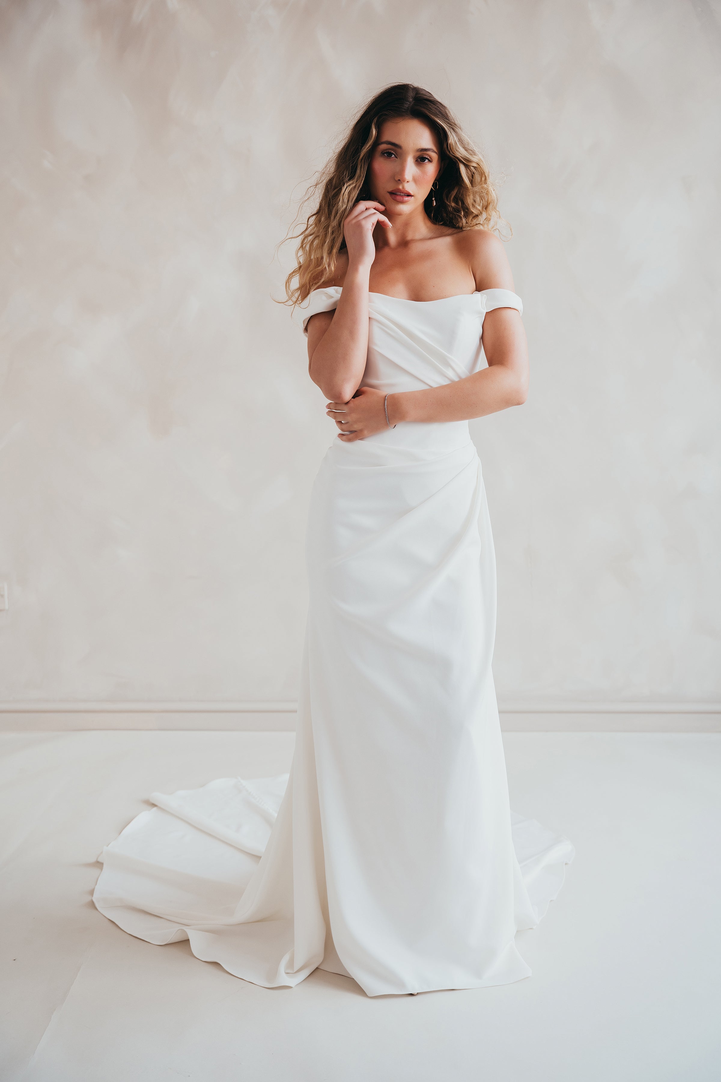 Bride wearing the Hadley off-the-shoulder stretch crepe wedding dress with draped neckline and button-back detail.