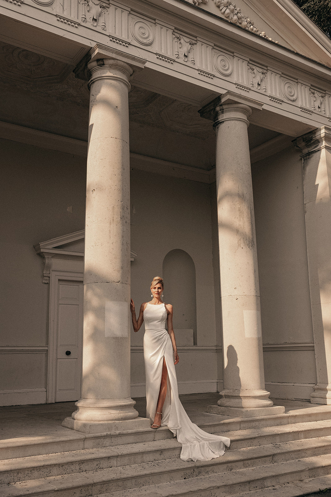 Woman in a ivory high neck wedding dress standing on steps with classical columns in the background